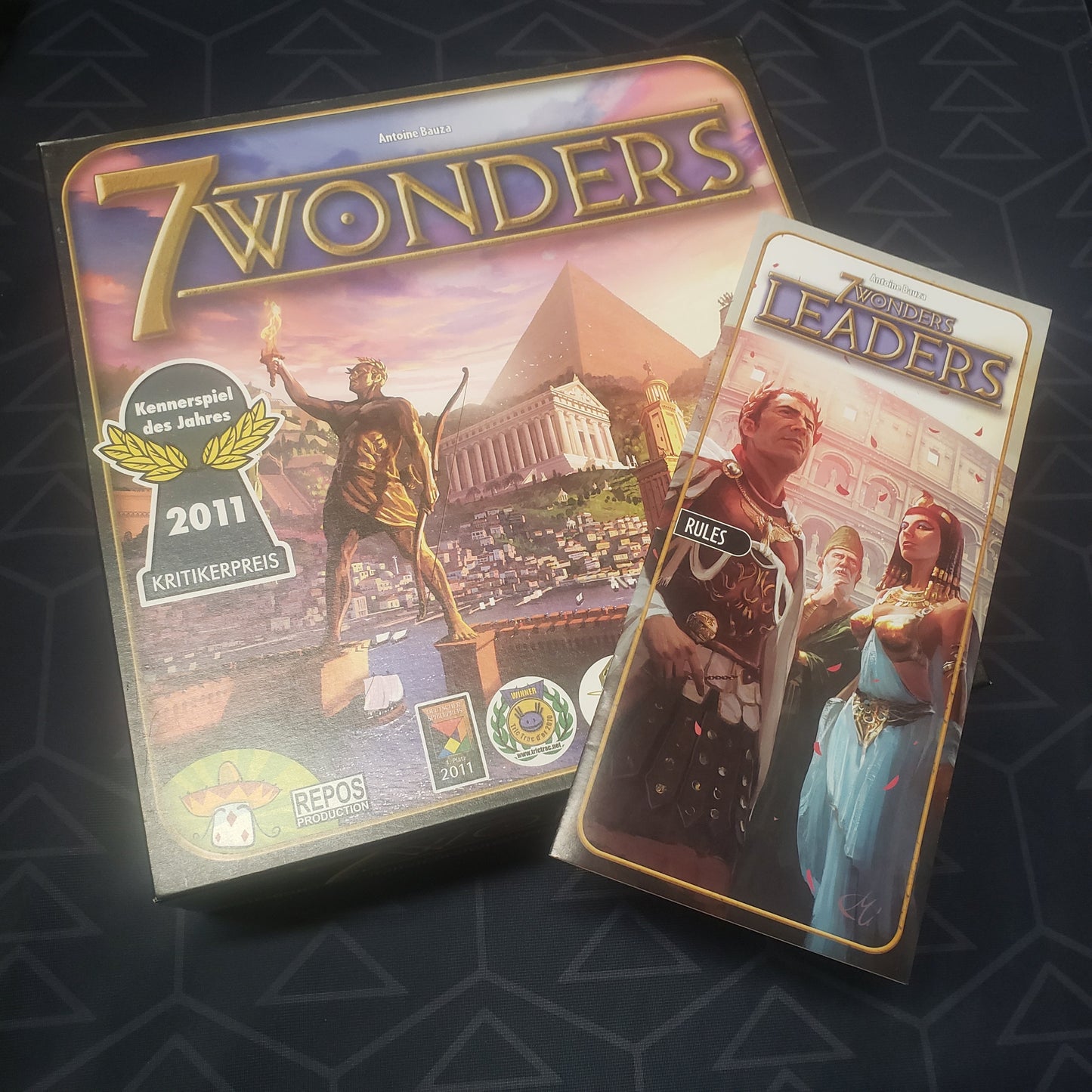 Image shows the front cover of the box of the 7 Wonders board game with the instructions for the Leaders expansion sitting on top of it