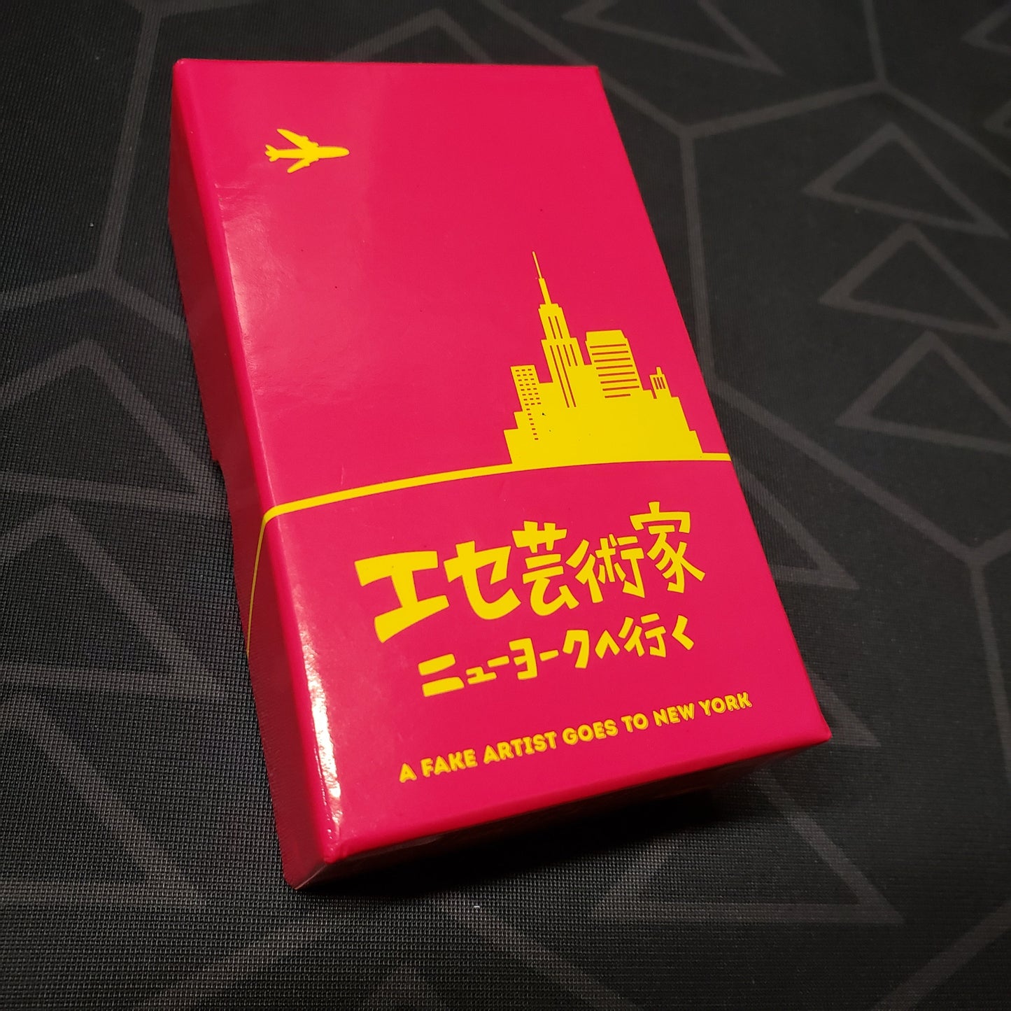 Image shows the front cover of the box of the multilingual edition of the board game A Fake Artist Goes to New York