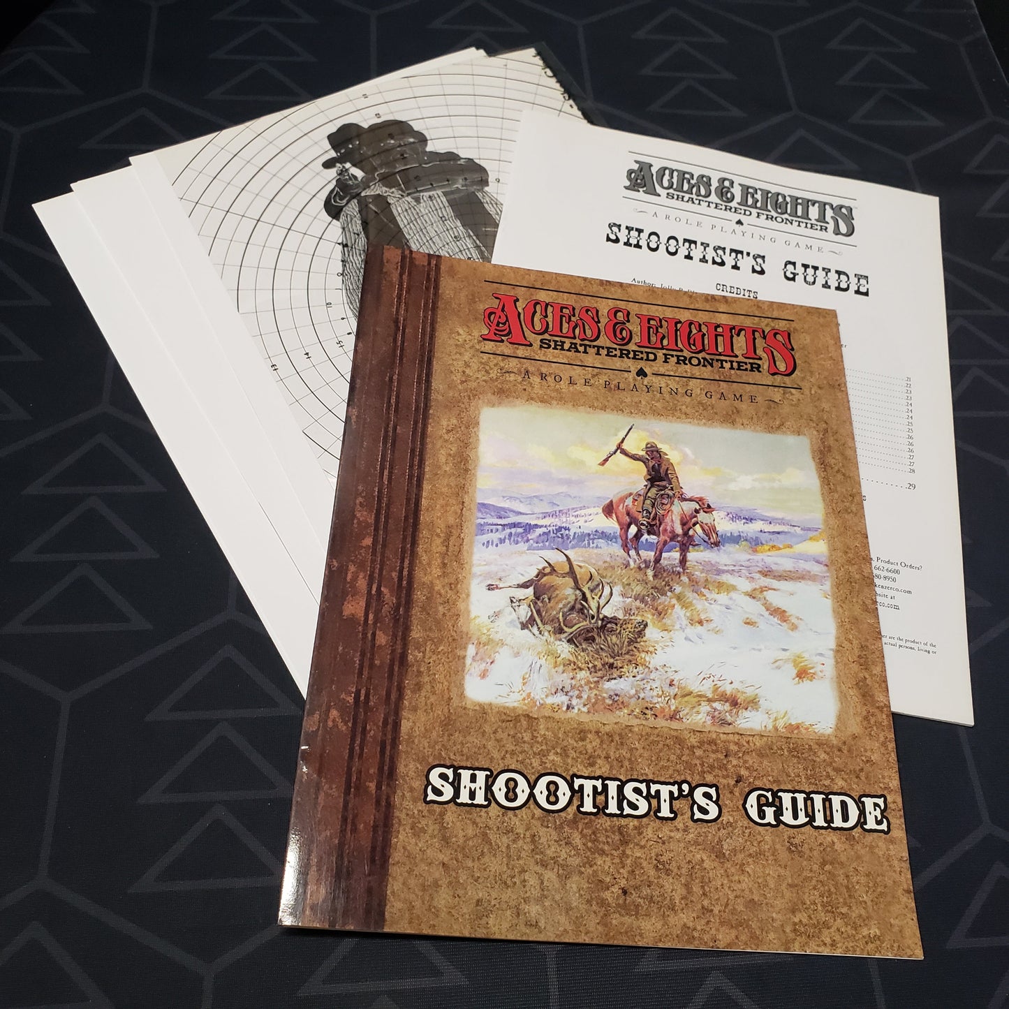 Image shows the front cover of the folio for the Shootist's Guide for the roleplaying game Aces & Eights: Shattered Frontier with the booklet and transparency fanned out