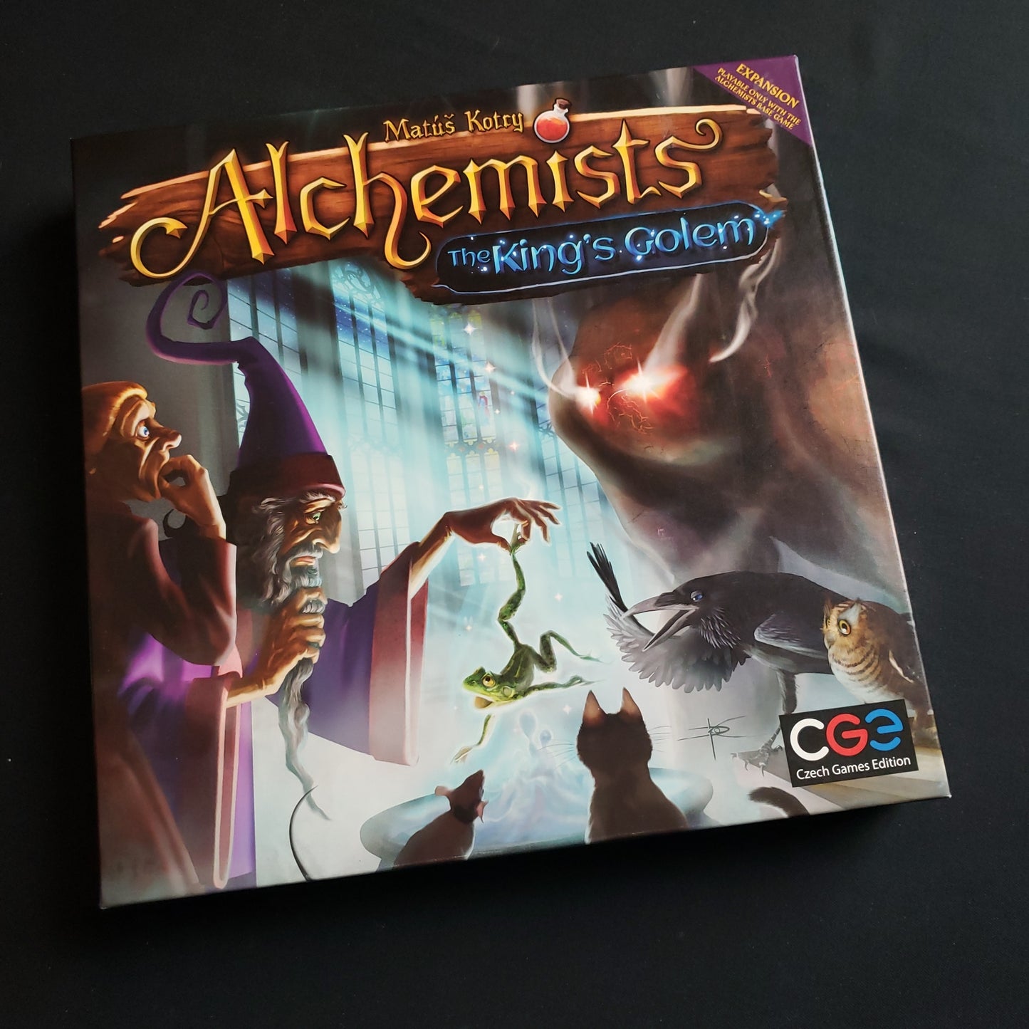 Image shows the front cover of the box of the King's Golem expansion for the board game Alchemists