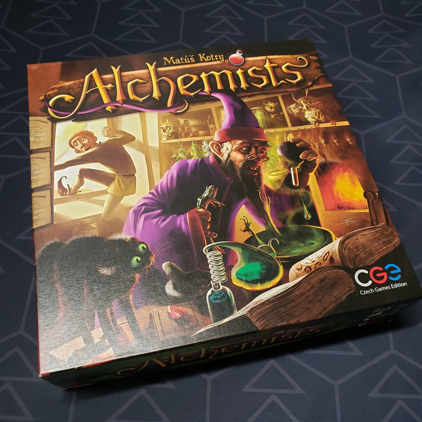 Image shows the front cover of the box of the Alchemists board game