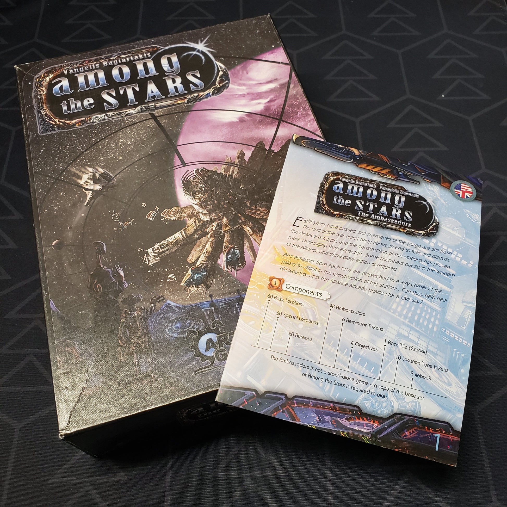 Image shows the front cover of the box of the Among the Stars board game with the instructions for the Ambassadors expansion sitting on top of it