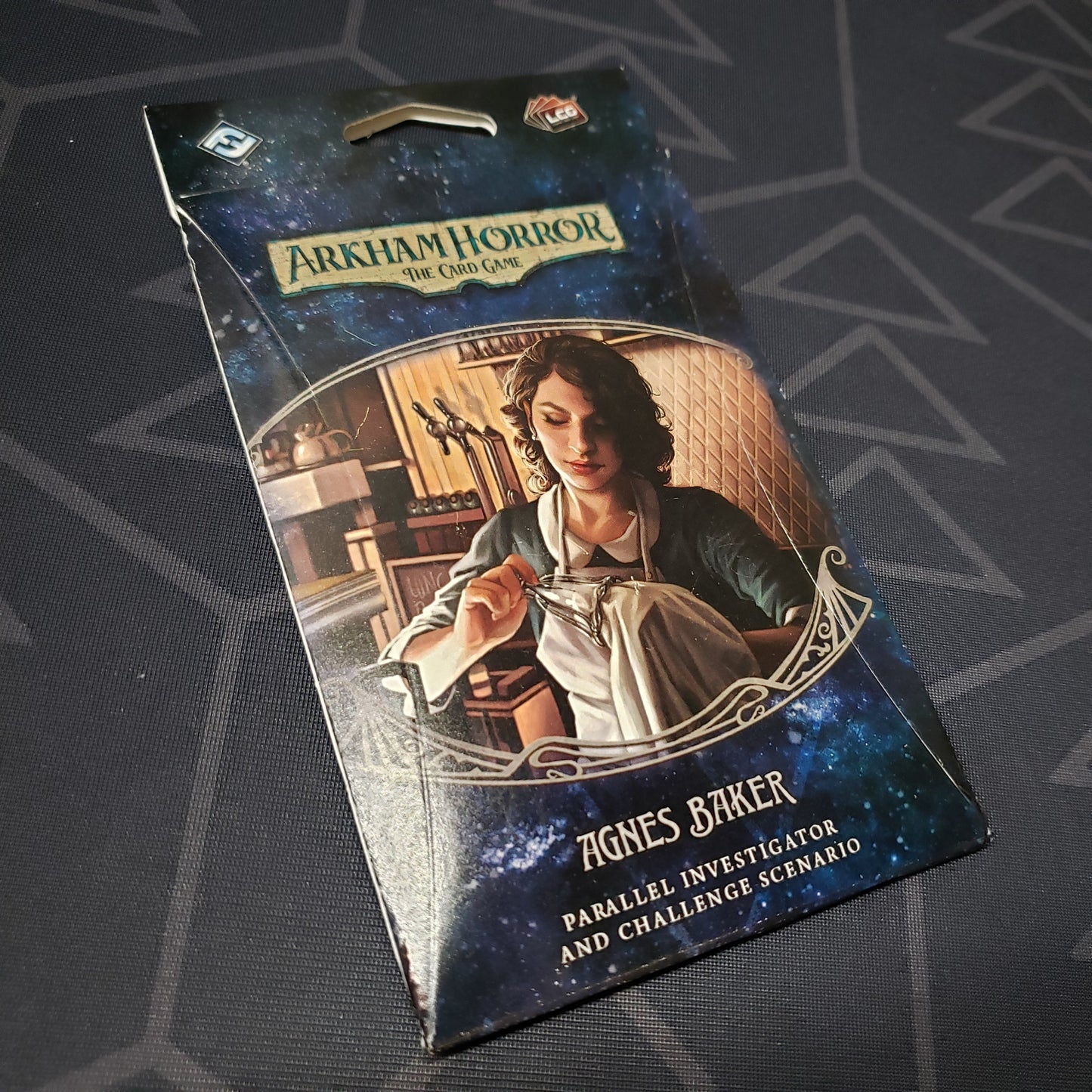 Image shows the front of the packaging of the Agnes Baker Parallel Investigator & Challenged Scenario expansion for Arkham Horror: The Card Game