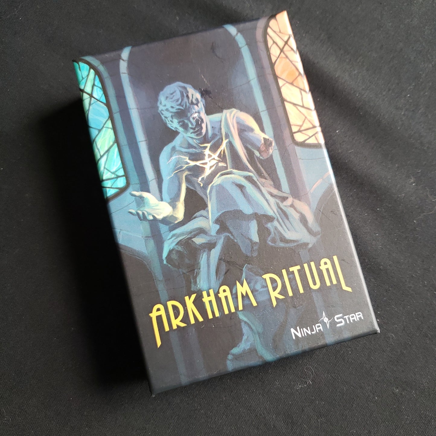 Image shows the front cover of the box of the Arkham Ritual card game
