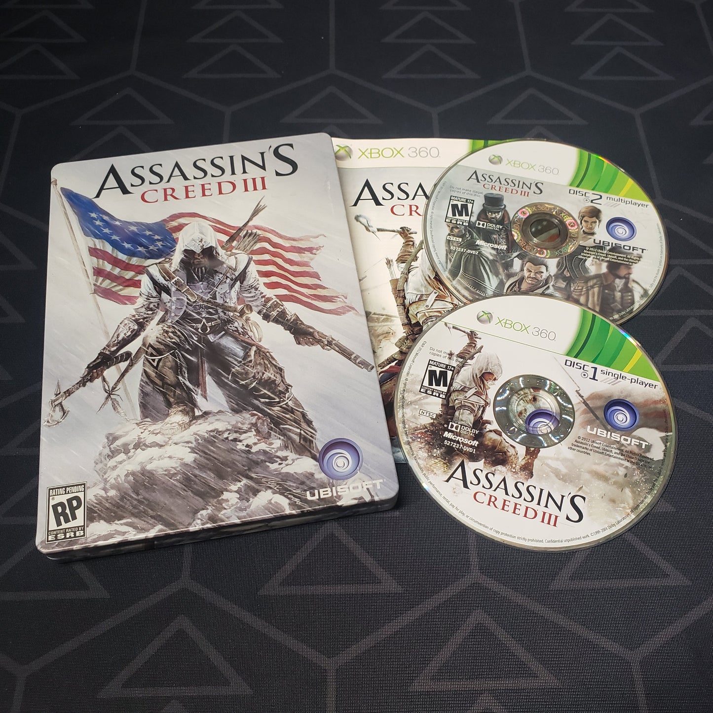 Image shows the steelbook case, manual & two discs for the video game Assassin's Creed III for Xbox 360