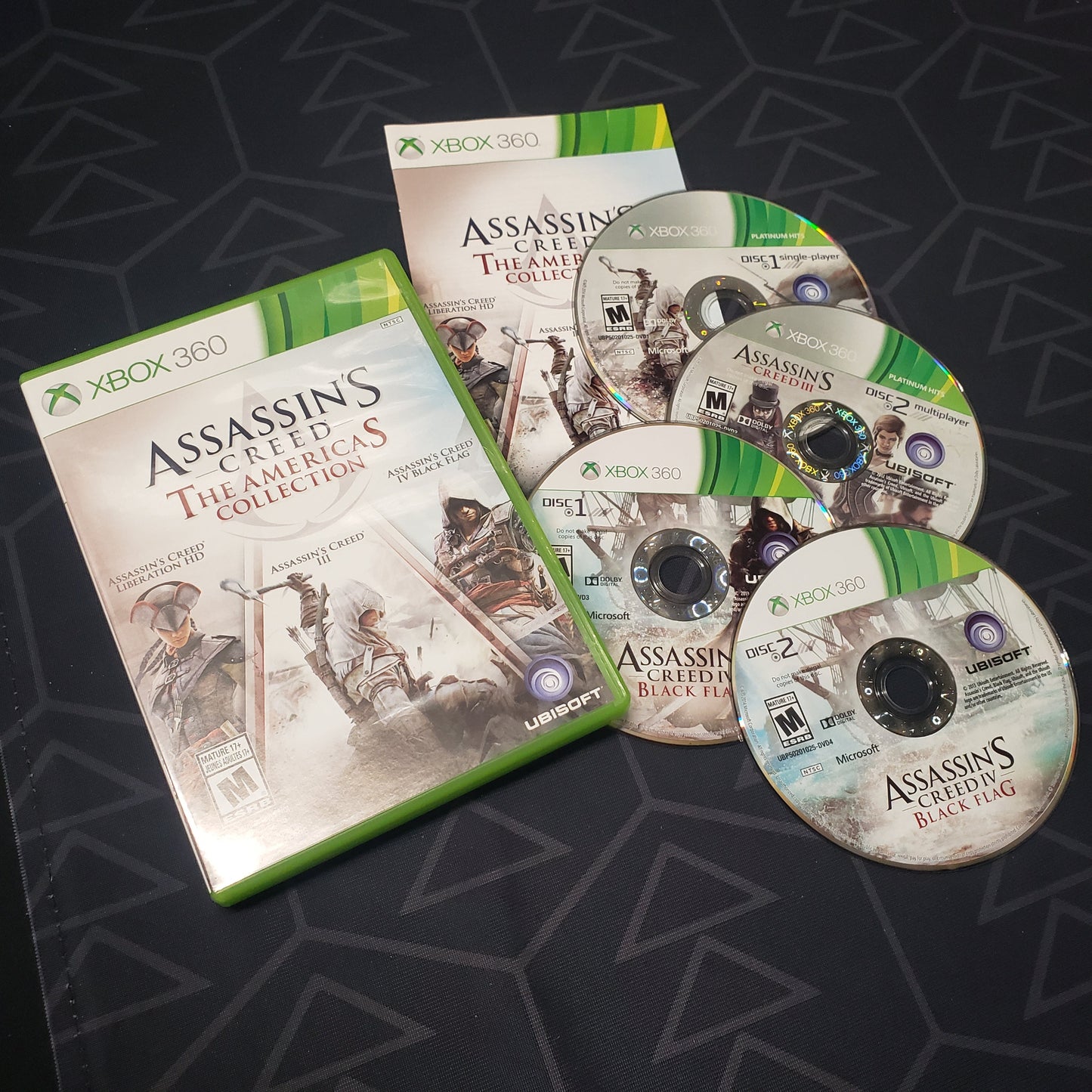 Image shows the case, manual and four discs for the video game Assassin's Creed: The Americas Collection for Xbox 360