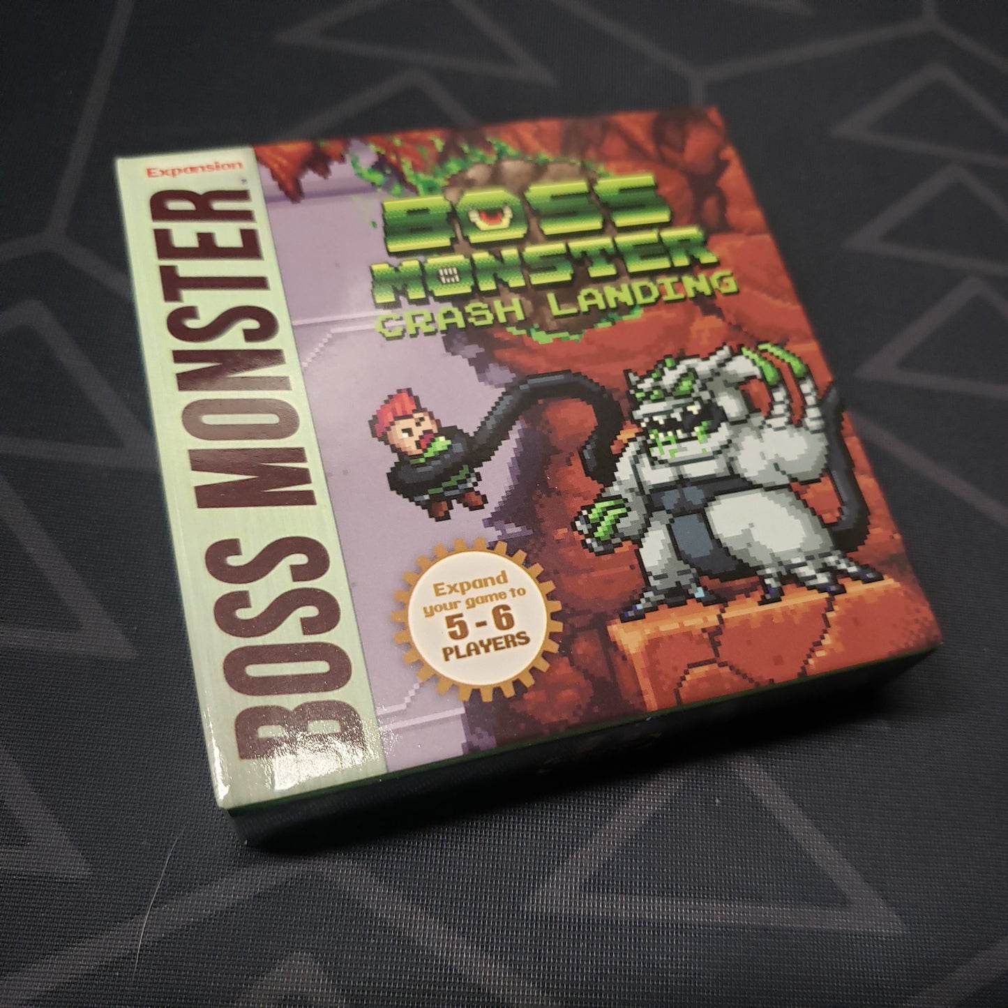 Image shows the front cover of the box of the Crash Landing expansion for the card game Boss Monster