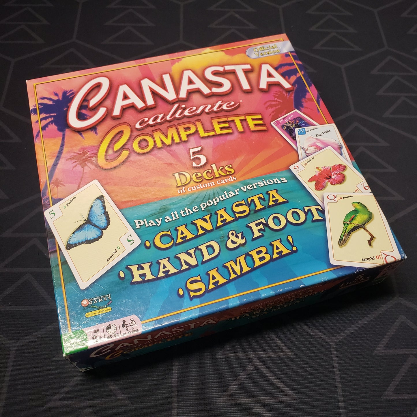 Image shows the front cover of the box for the Canasta Caliente Complete card game