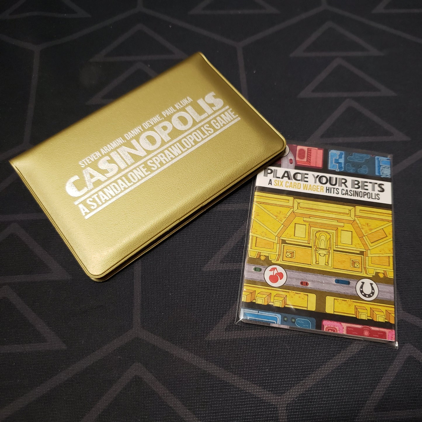 Image shows the front of the card wallet for the Casinopolis card game, with the Place Your Bets expansion sitting next to it