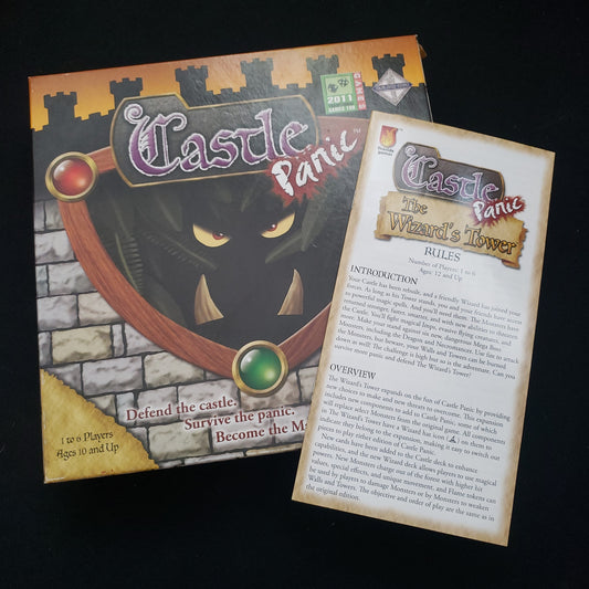 Image shows the front cover of the box of the Castle Panic board game, with the instructions for the Wizard's Tower expansion sitting on top of it