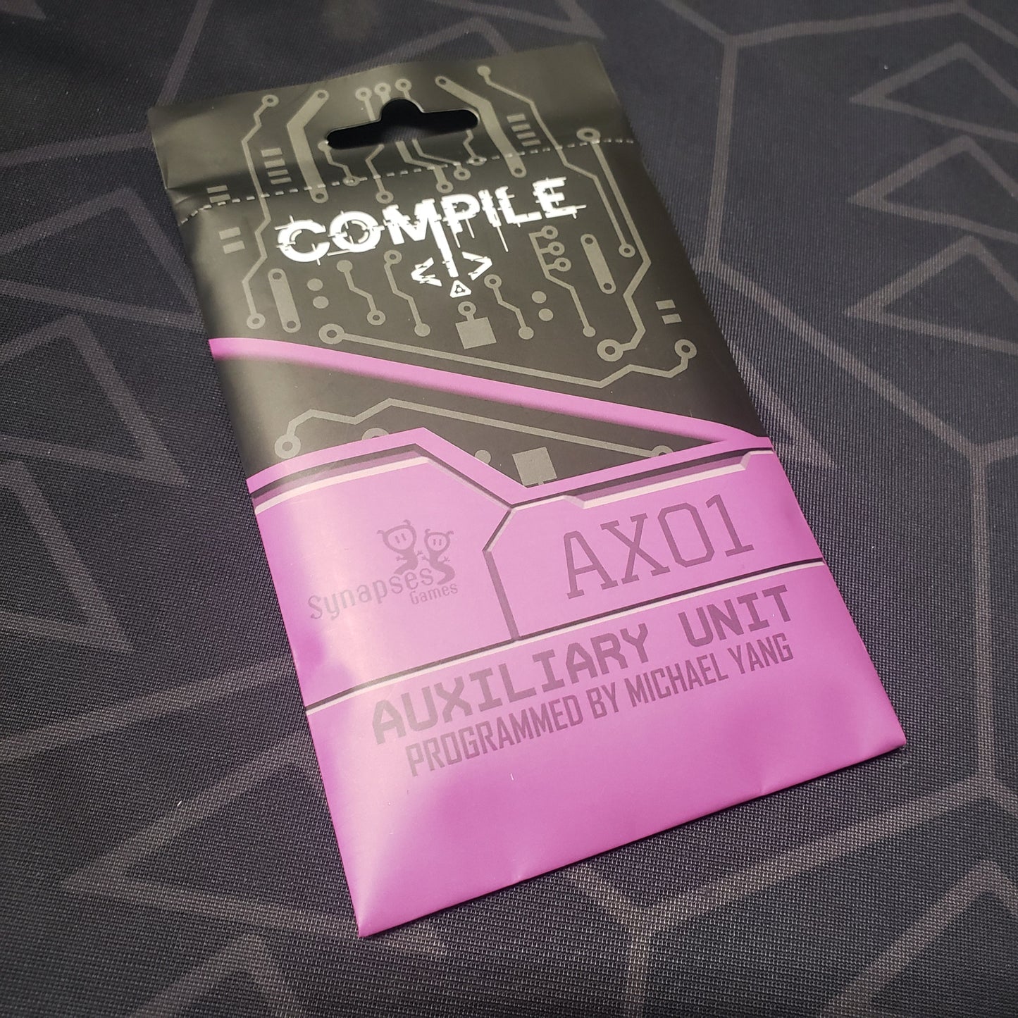 Image shows the front of teh packaging of the Aux 1 expansion for the card game Compile
