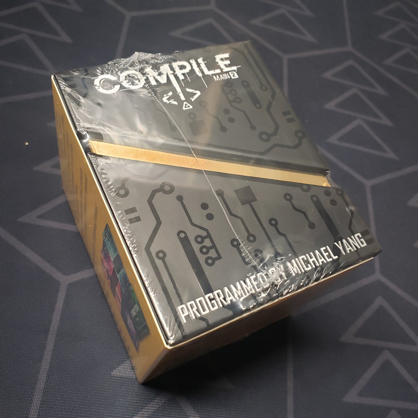Image shows the front cover of the box for the card game Compile: Main 2