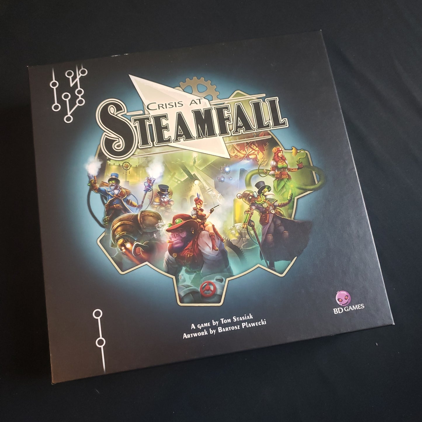 Image shows the front cover of the box of the Crisis At Steamfall board game