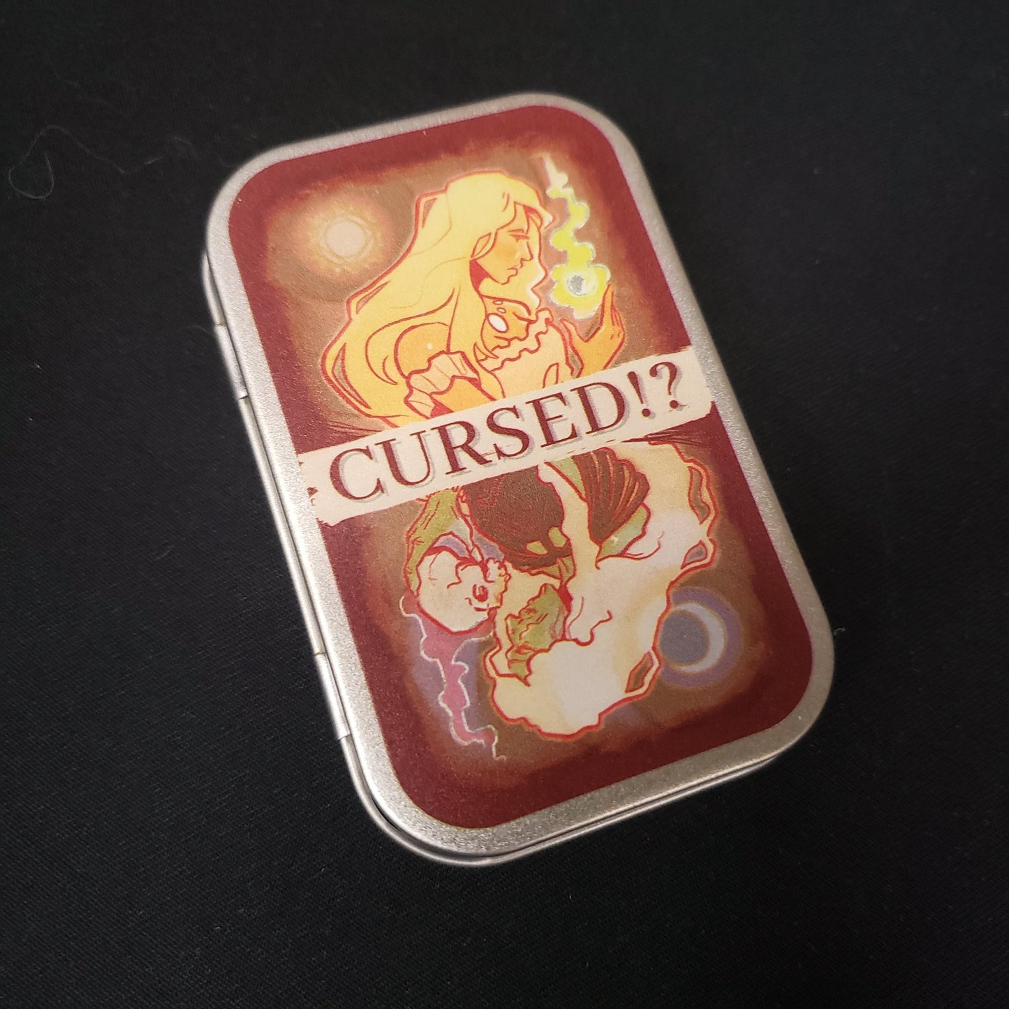 Image shows the front cover of the tin of the Cursed!? card game