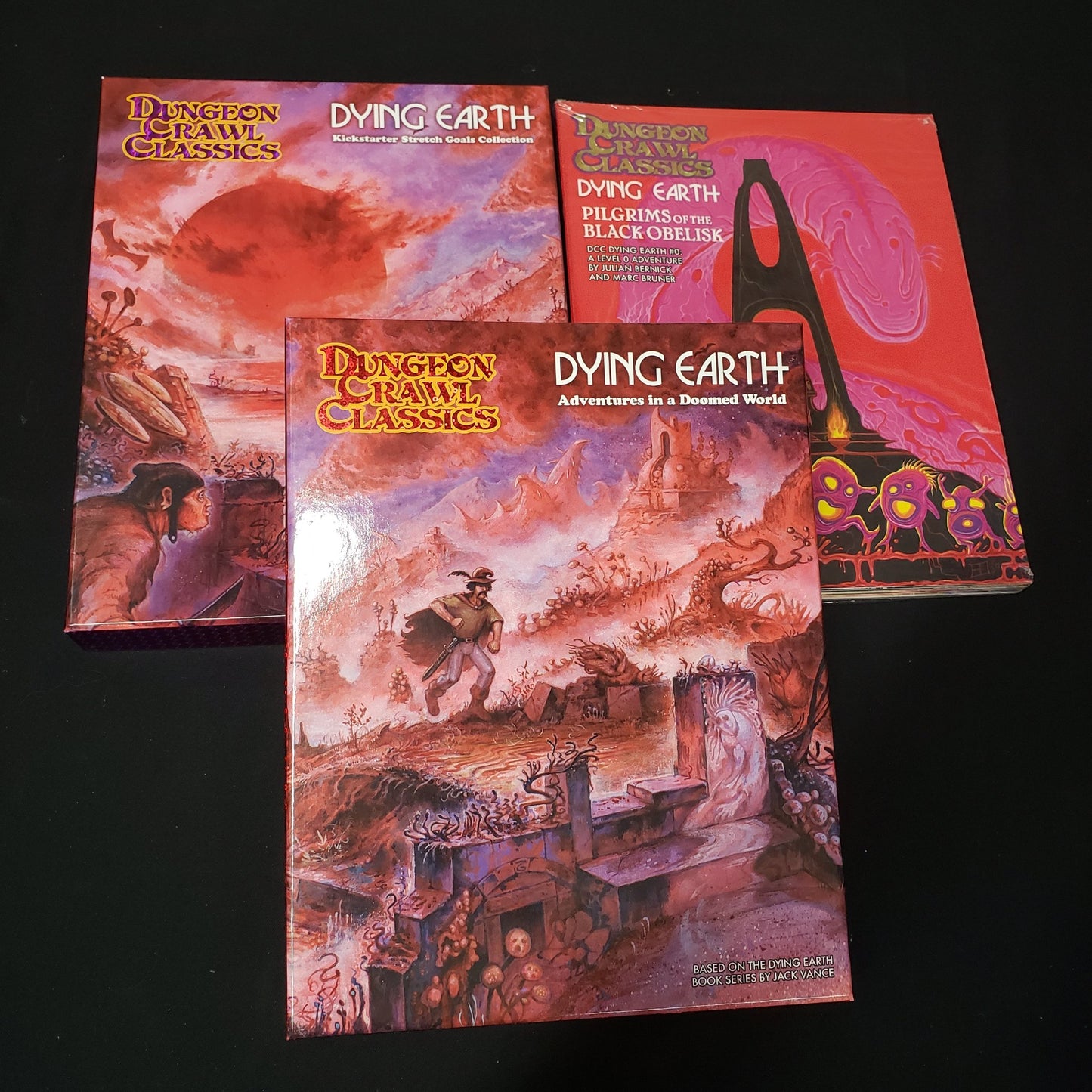 Image shows the front covers of the boxes of the Dying Earth base game, Stretch Goals box, and Adventure Module bundle.