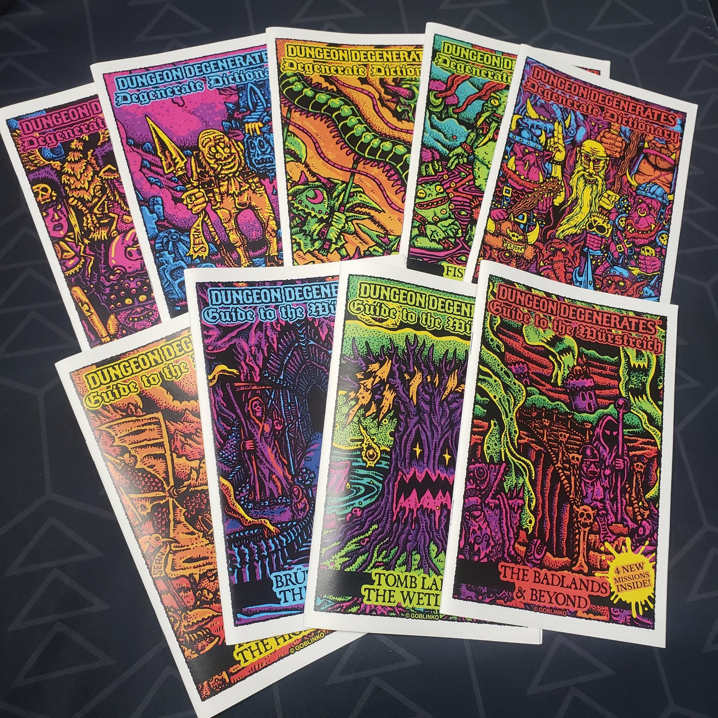 Image shows the front cover of the nine zines that make up the Lore Book Bundle for the board game Dungeon Degenerates