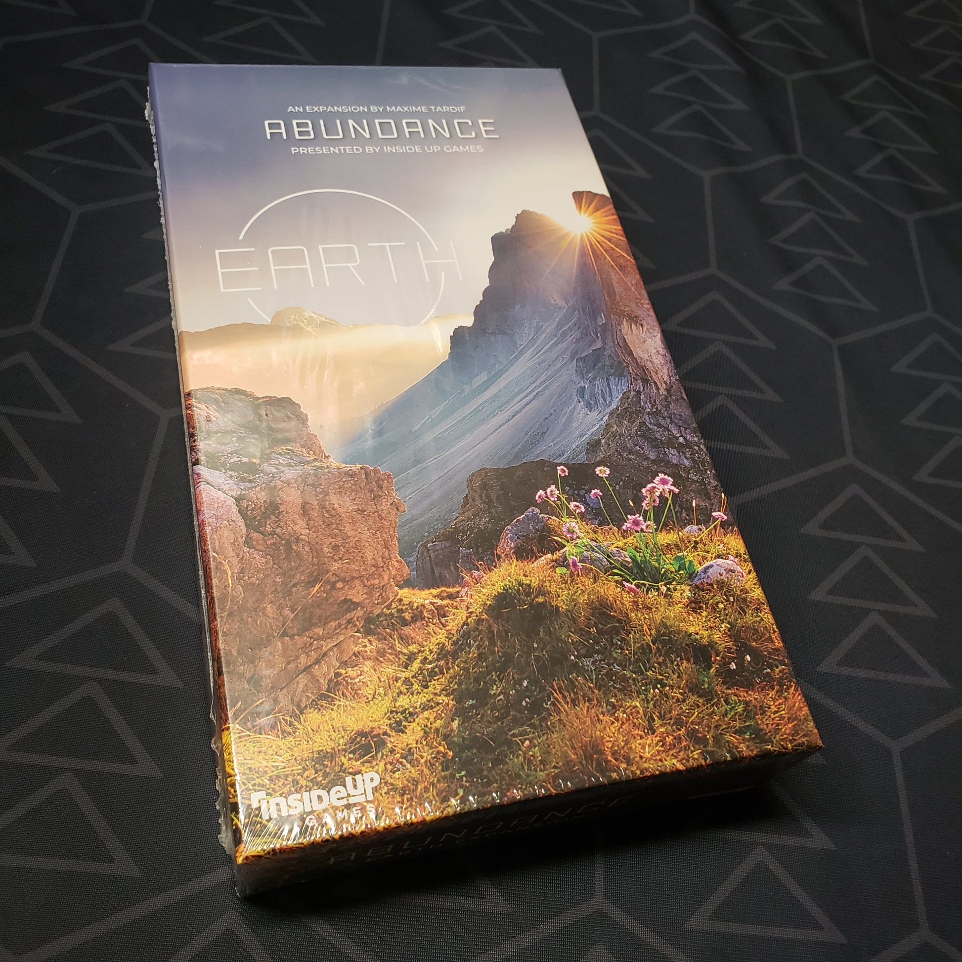 Image shows the front cover of the box of the Abundance expansion for the board game Earth