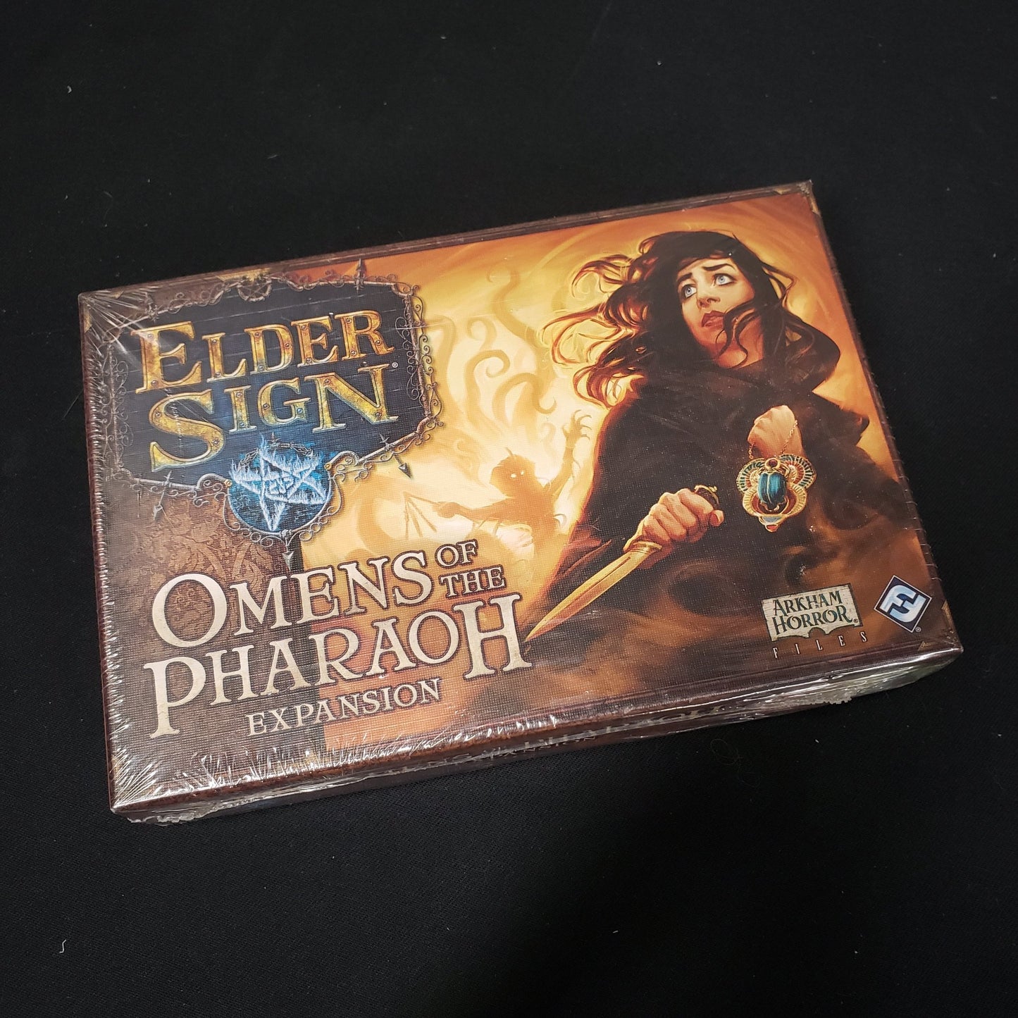 Image shows the front cover of the box for the Omens of the Pharaoh expansion from the board game Elder Sign