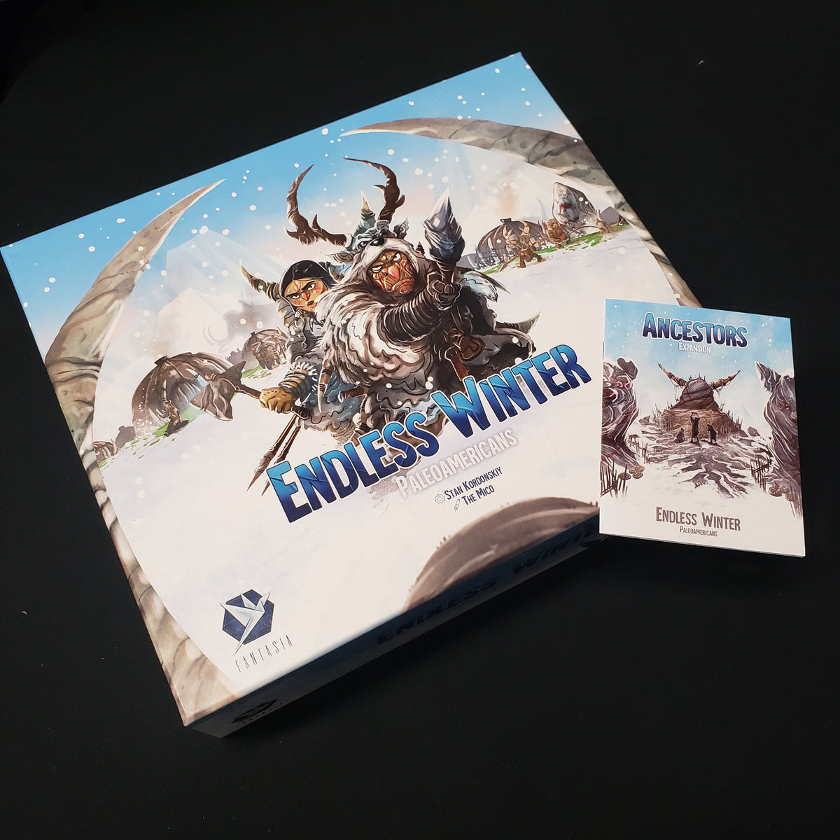 Image shows the front cover of the box for the Endless Winter: Paleoamericans board game with the instructions for the Ancestors expansion sitting on top of it