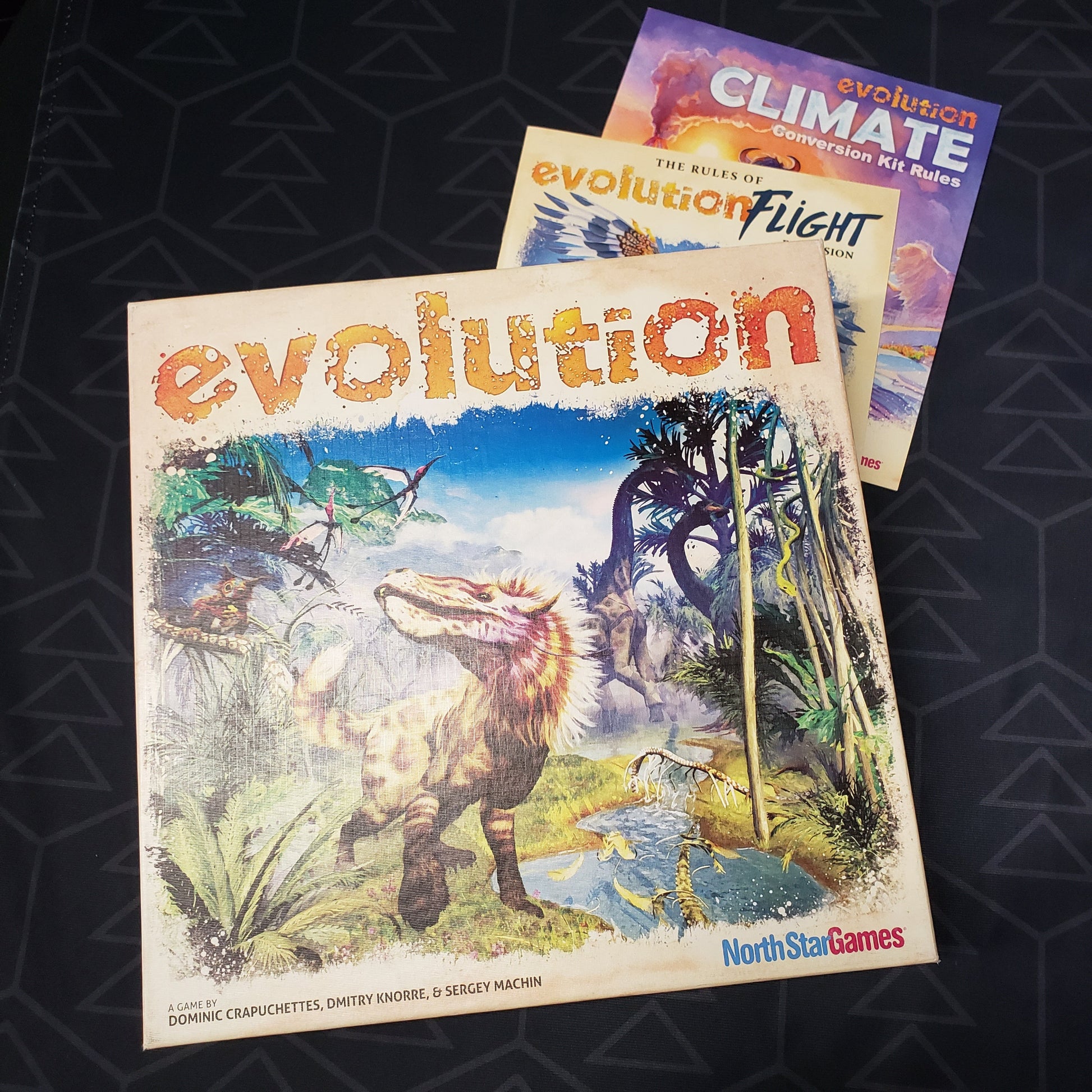 Image shows the front cover of the box of the Evolution card game sitting on top of the instructions for the Flight & Climate expansions
