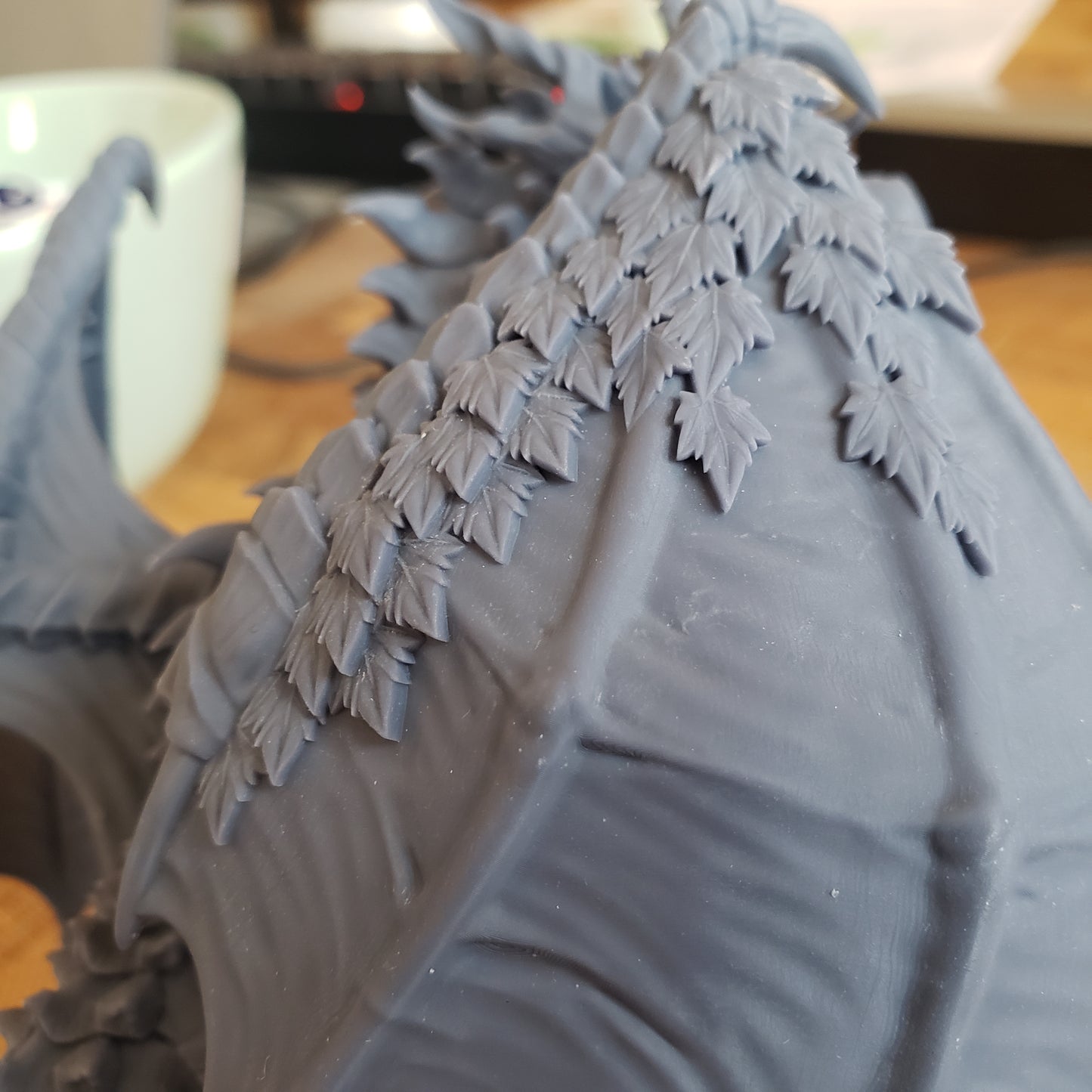 Image is a photo of the wing of a 3D printed forest dragon gaming miniature printed in-house at All Systems Go
