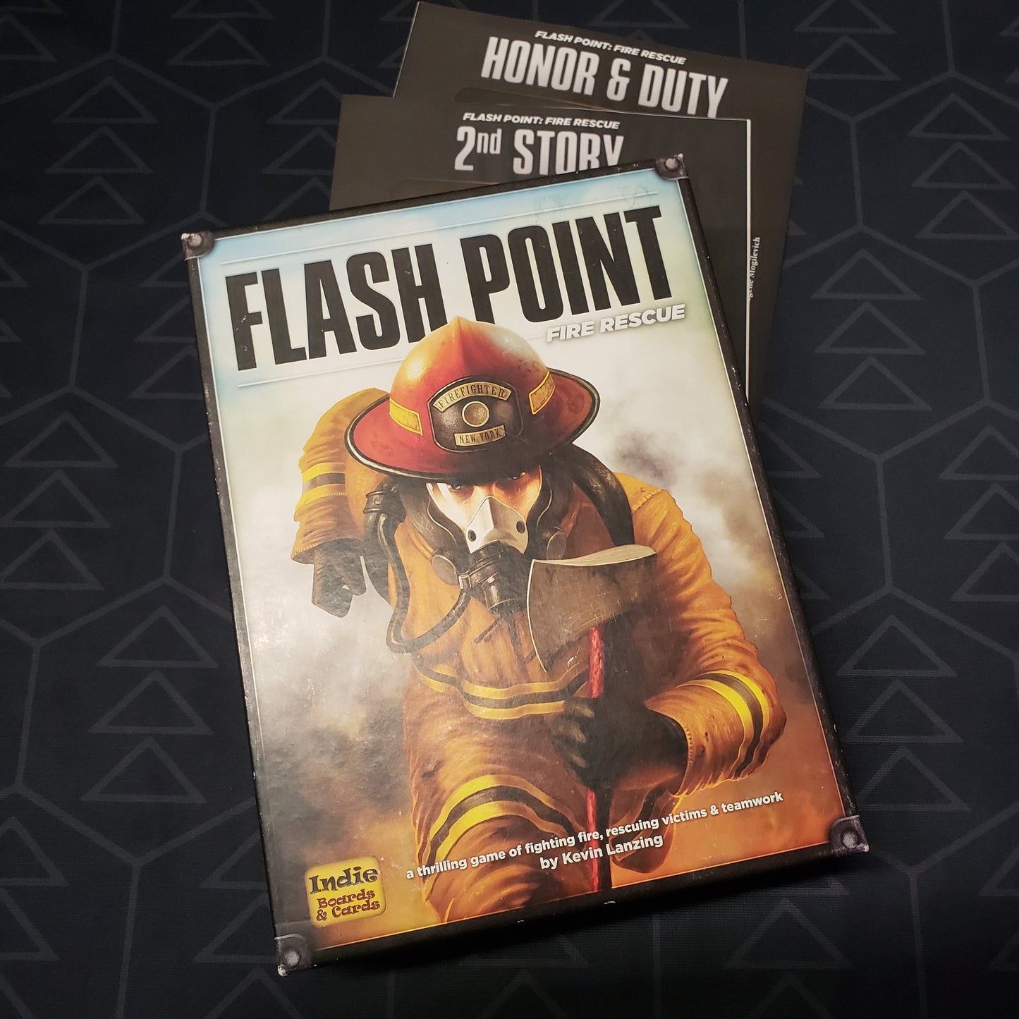 Image shows the front cover of the box of the Flash Point: Fire Rescue board game with the instruction sheets for the 2nd Story and Honor & Duty expansions