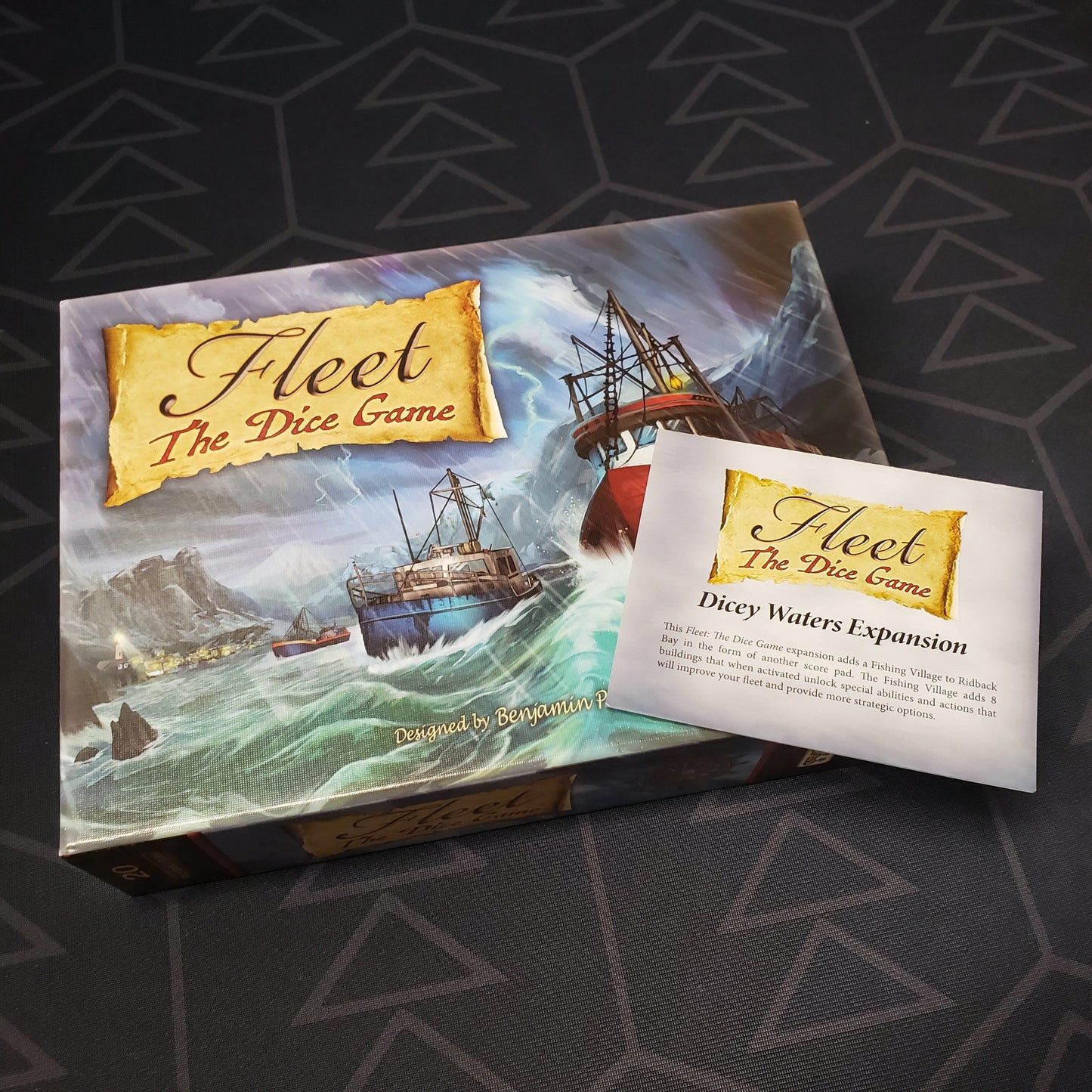 Image shows the front cover of the box for the board game Fleet: The Dice Game with the instructions for the Dicey Waters expansion sitting on top of it