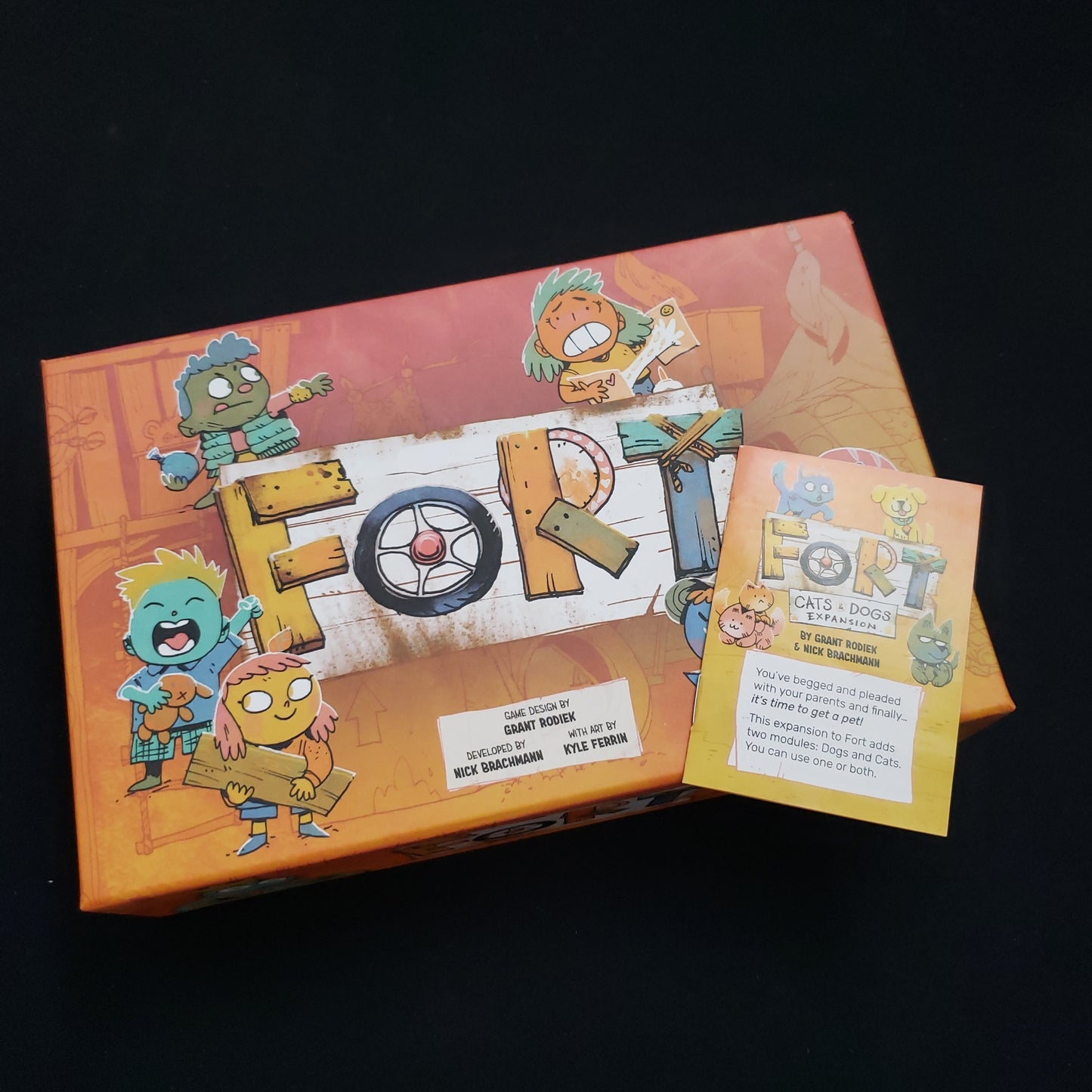 Image shows the front cover of the box of the Fort card game, with the instructions for the Cats & Dogs expansion sitting on top of it