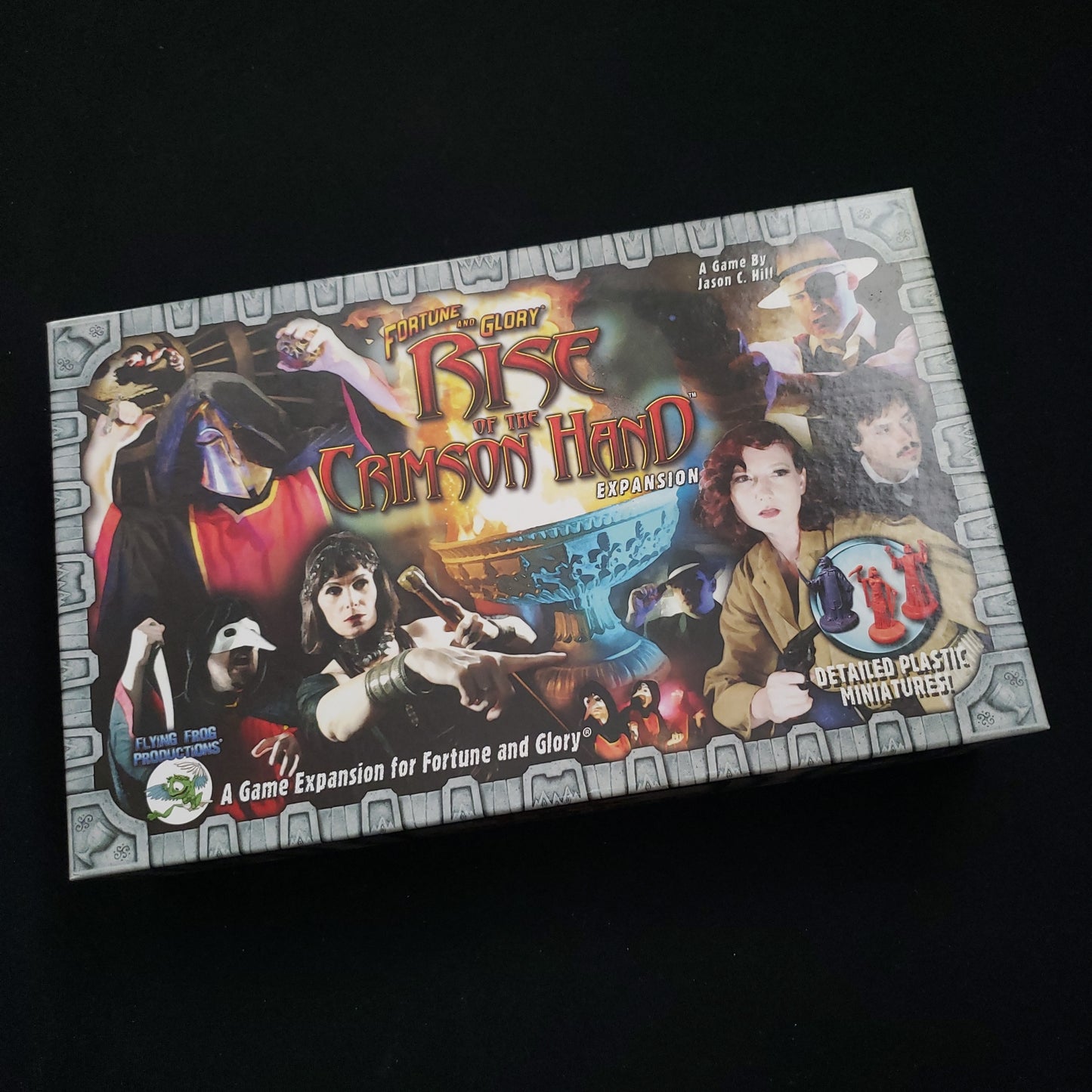 Image shows the front cover of the box of the Rise of the Crimson Hand expansion for the board game Fortune & Glory