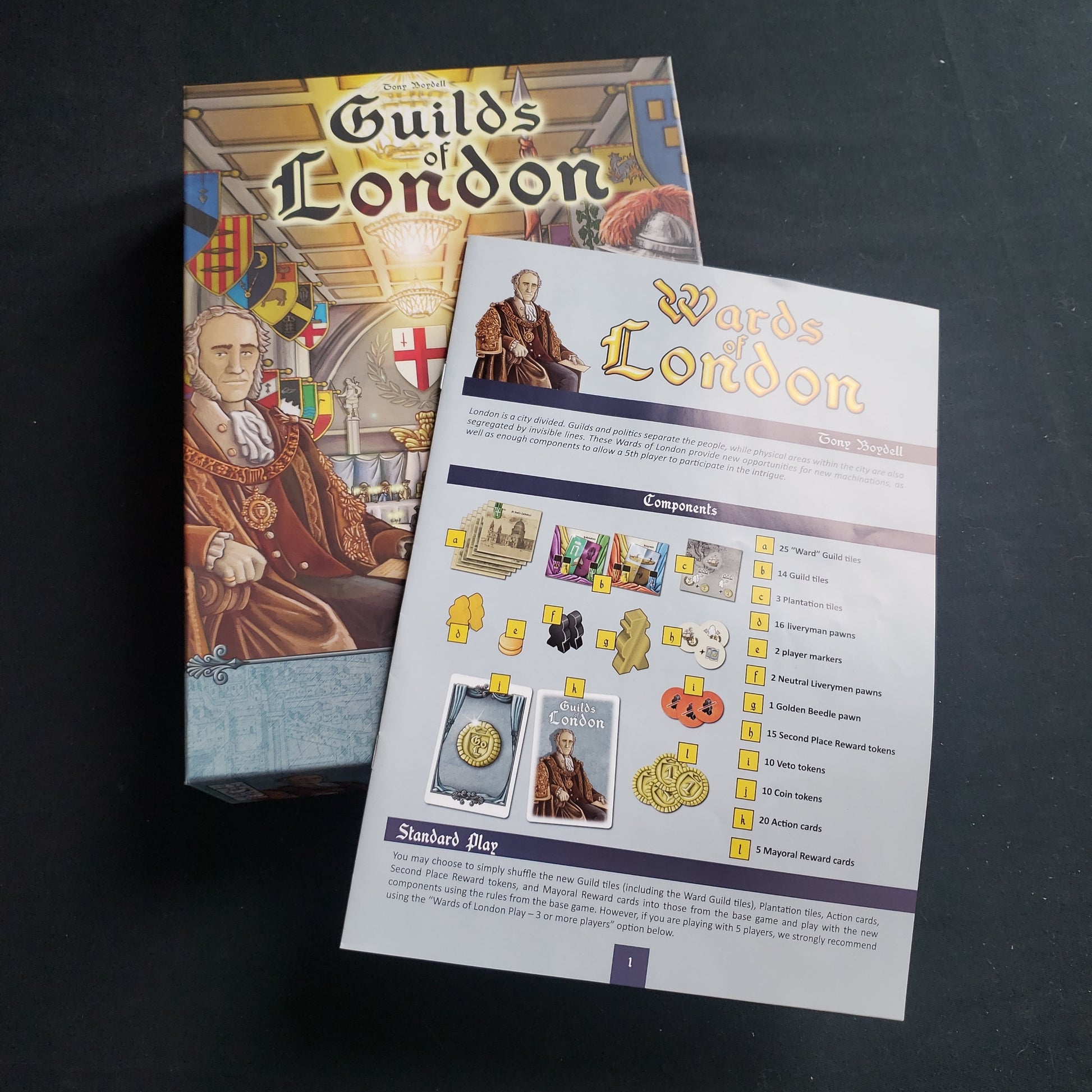 Image shows the front cover of the box of the Guilds of London board game, with the instructions for the Wards of London expansion sitting on top of it
