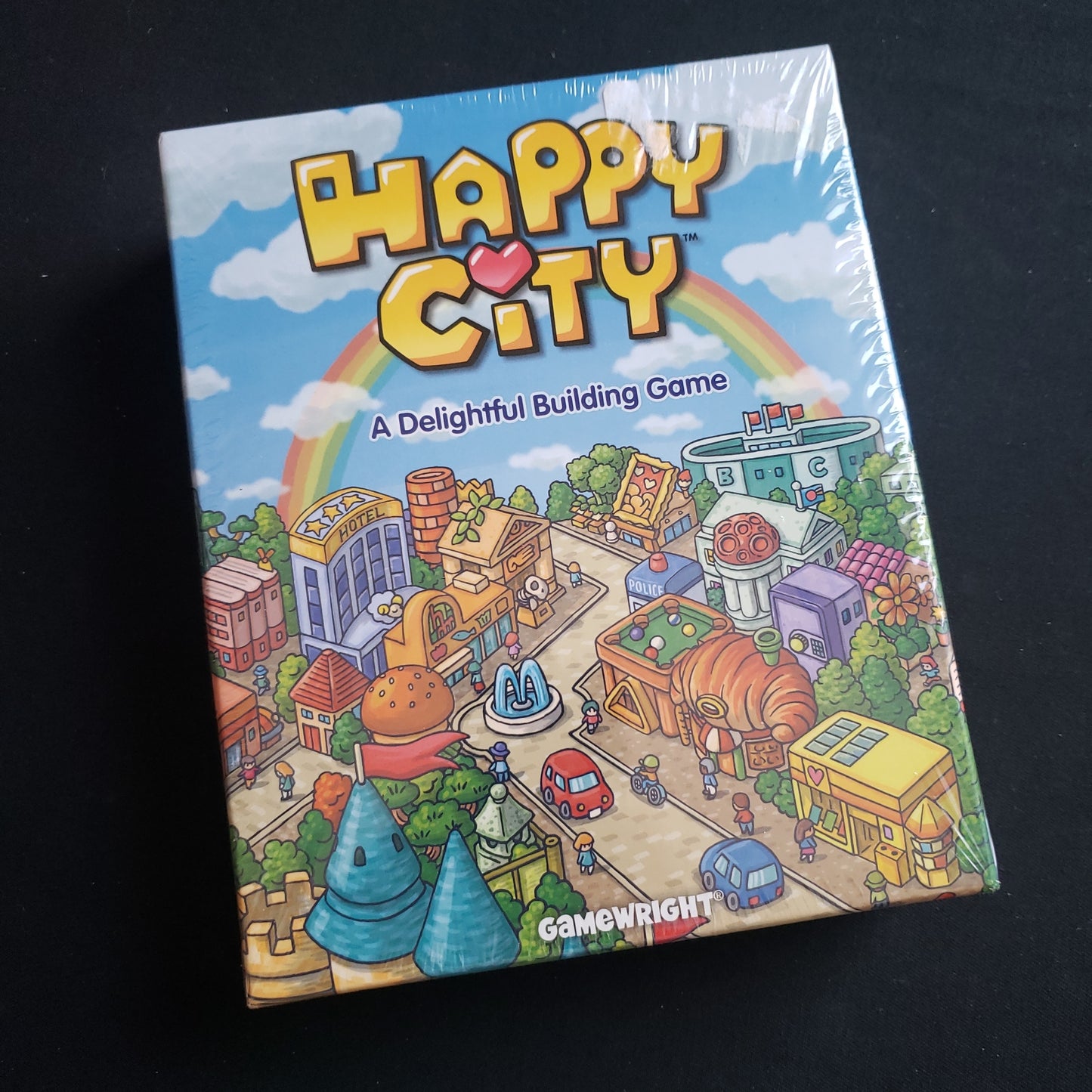 Image shows the front cover of the box of the Happy City board game