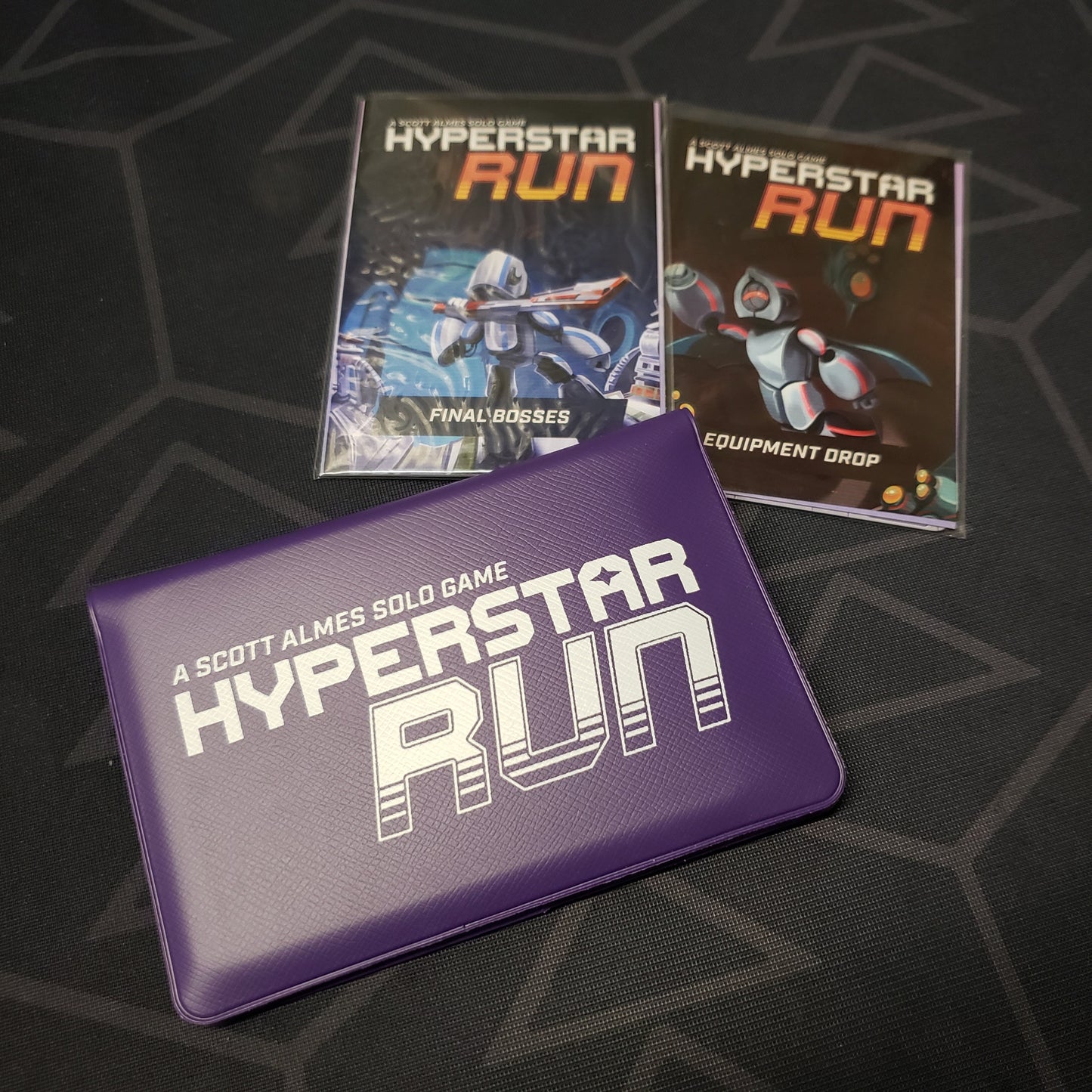 Image shows the front of the card wallet for the Hyperstar Run card game with the Final Bosses and Equipment Drop expansions sitting next to it
