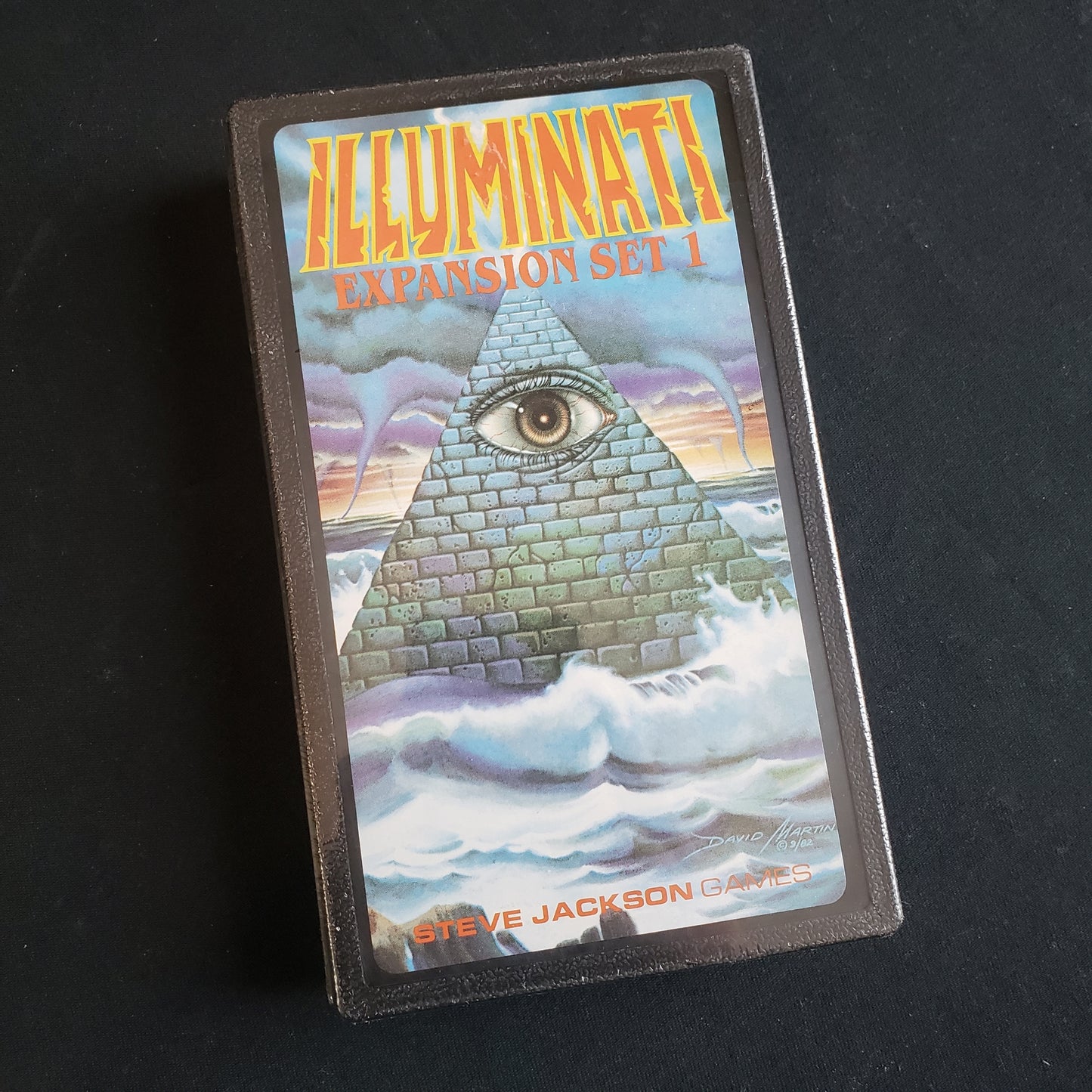 Image shows the front cover of the box of the first expansion set for the card game Illuminati