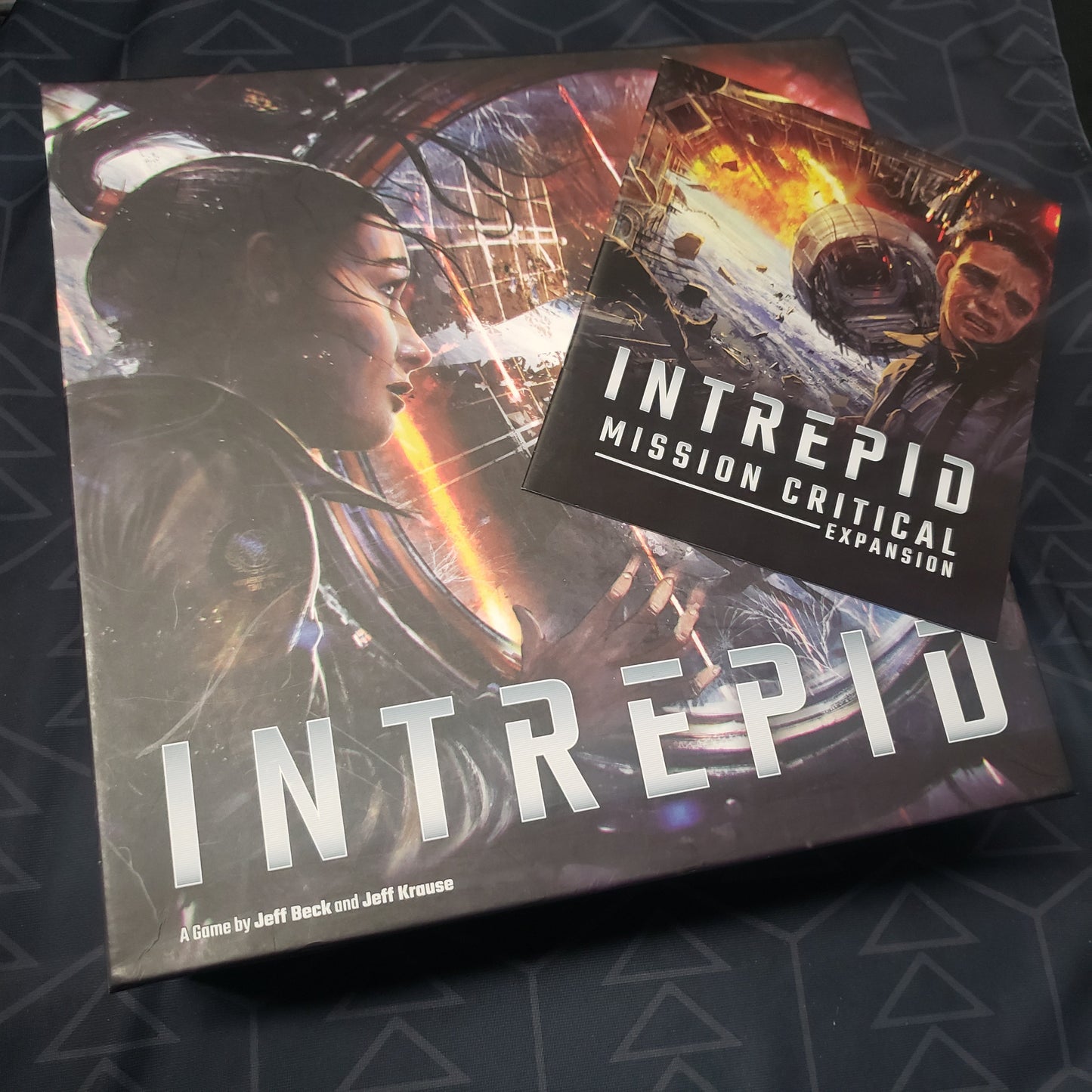 Image shows the front cover of the box for the Intrepid board game with the expansion instructions sitting on top of it