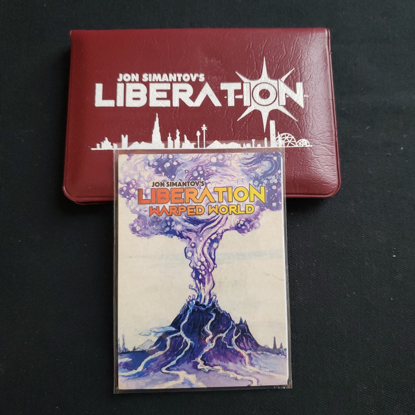 Image shows the front cover of the package for the Liberation card game, with the Warped World expansion sitting on top of it