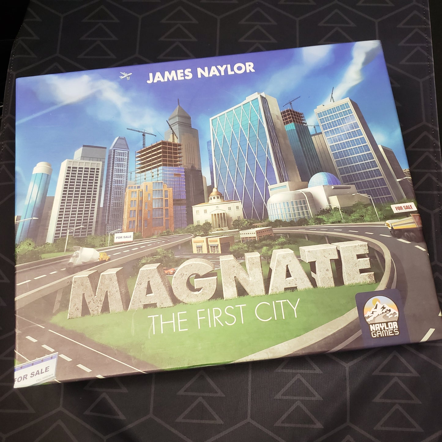 Image shows the front cover of the box of the board game Magnate: The First City