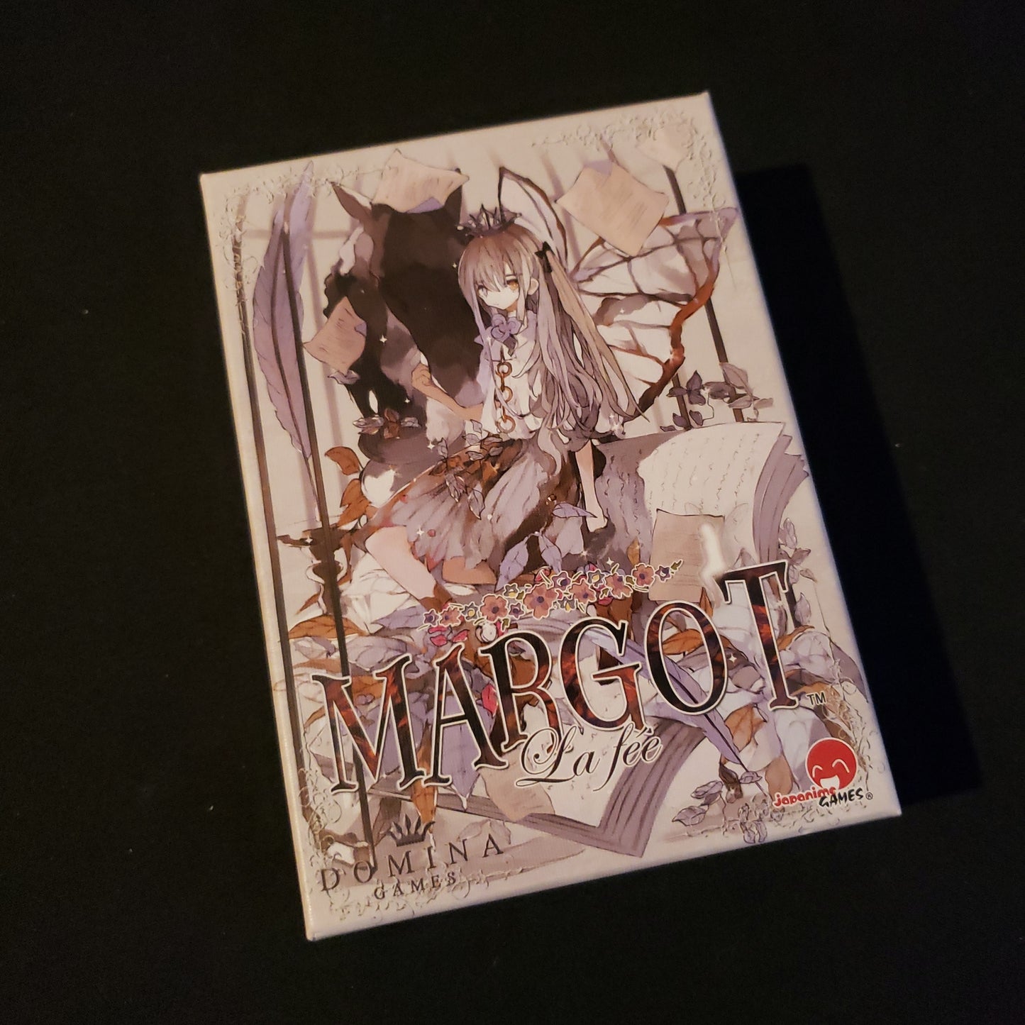 Image shows the front cover of the box of the card game Margot: La fee