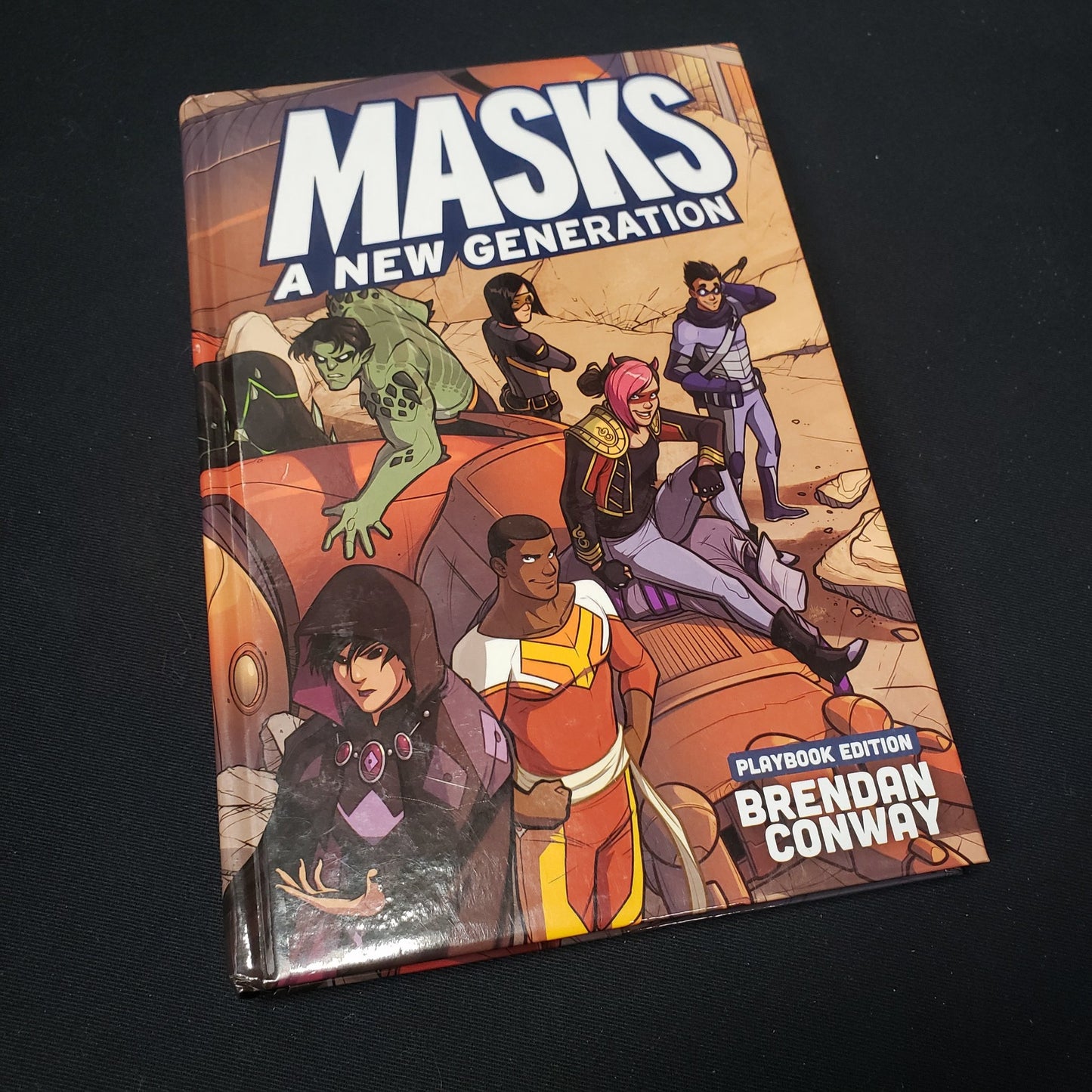 Image shows the front cover of the core rulebook for the roleplaying game Masks: A New Generation