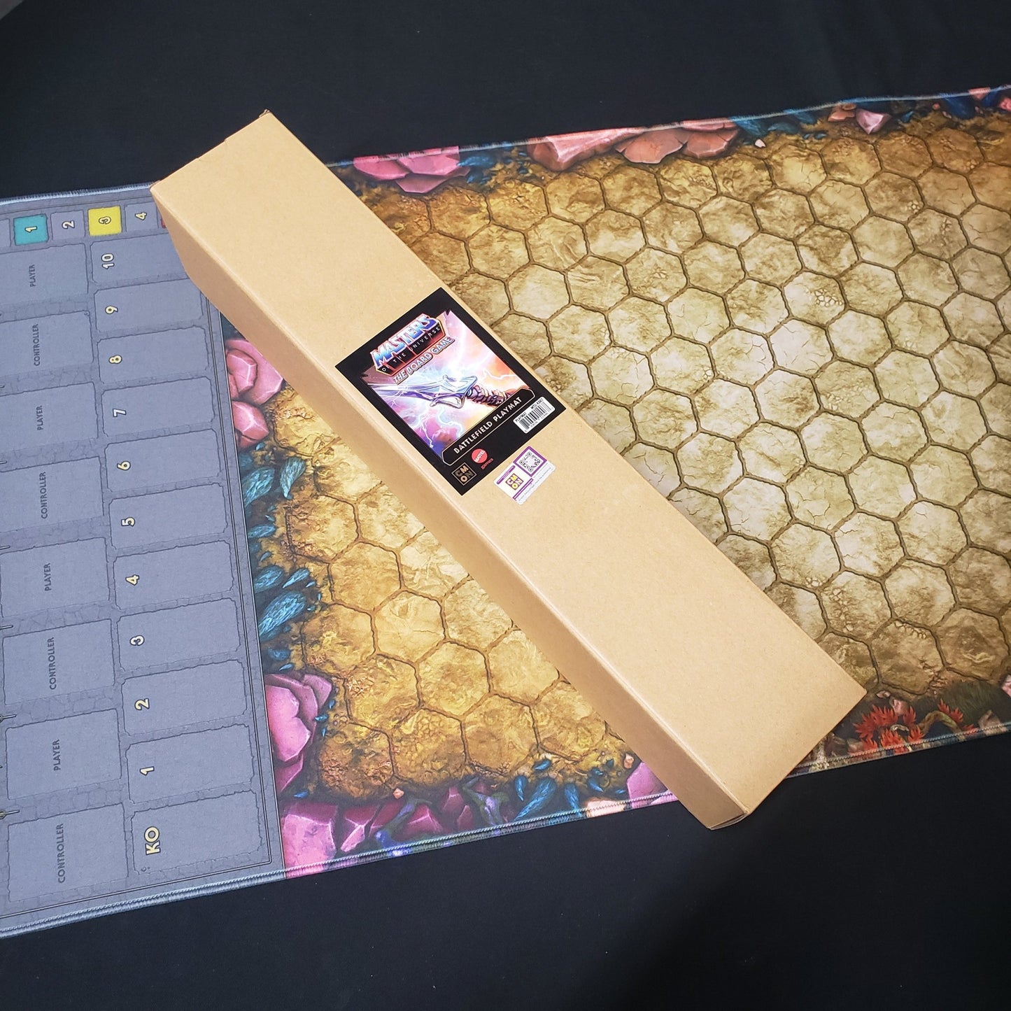 Image shows the box for the playmat for the Masters of the Universe: Clash for Eternia board game sitting on top of the nrolled playmat