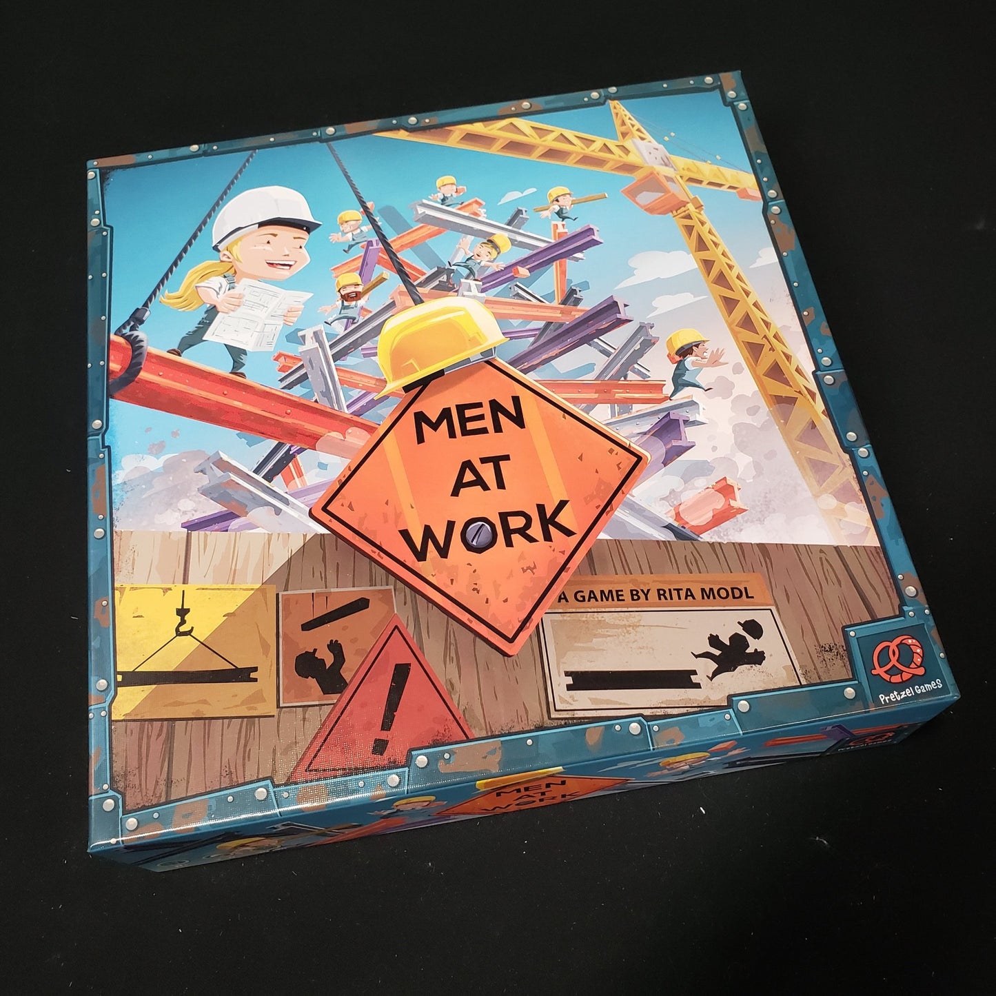 Image shows the front cover of the box of the Men At Aork board game