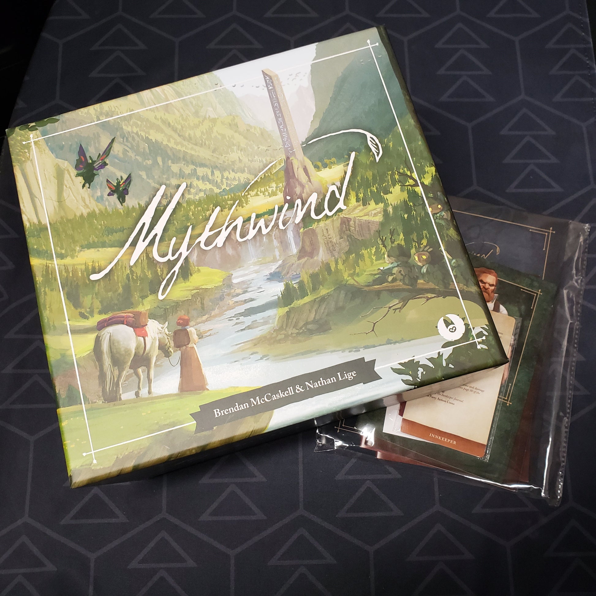 Image shows the front cover of the box for the Mythwind board game sitting on top of the revised rules bundle