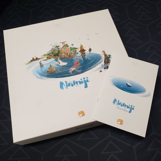 Image shows the front cover of the box for the Namiji board game with the instructions for the Aquamarine expansion sitting on top of it