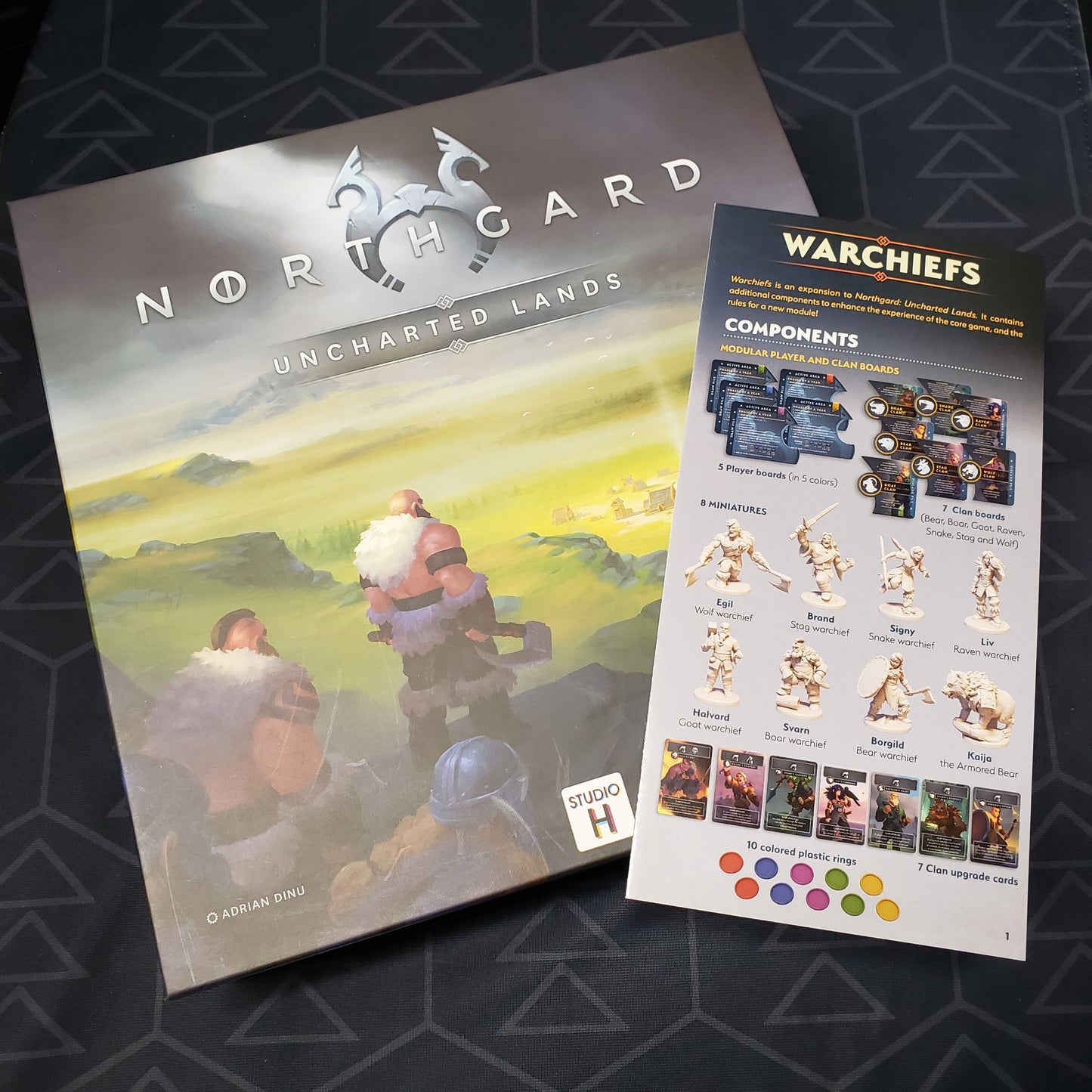 Image shows the front cover of the box of the board game Northgard: Uncharted Lands with the instructions for the Warchiefs expansion sitting on top of it