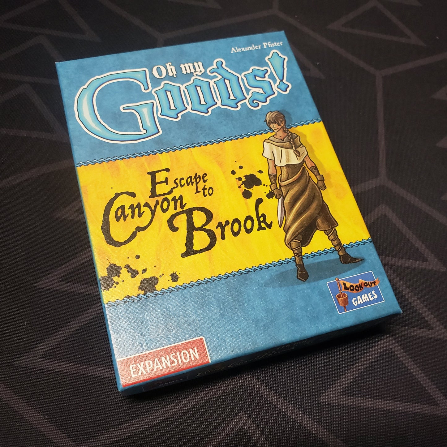 Image shows the front cover of the box of the Escape to Canyon Brook expansion for the card game Oh My Goods!