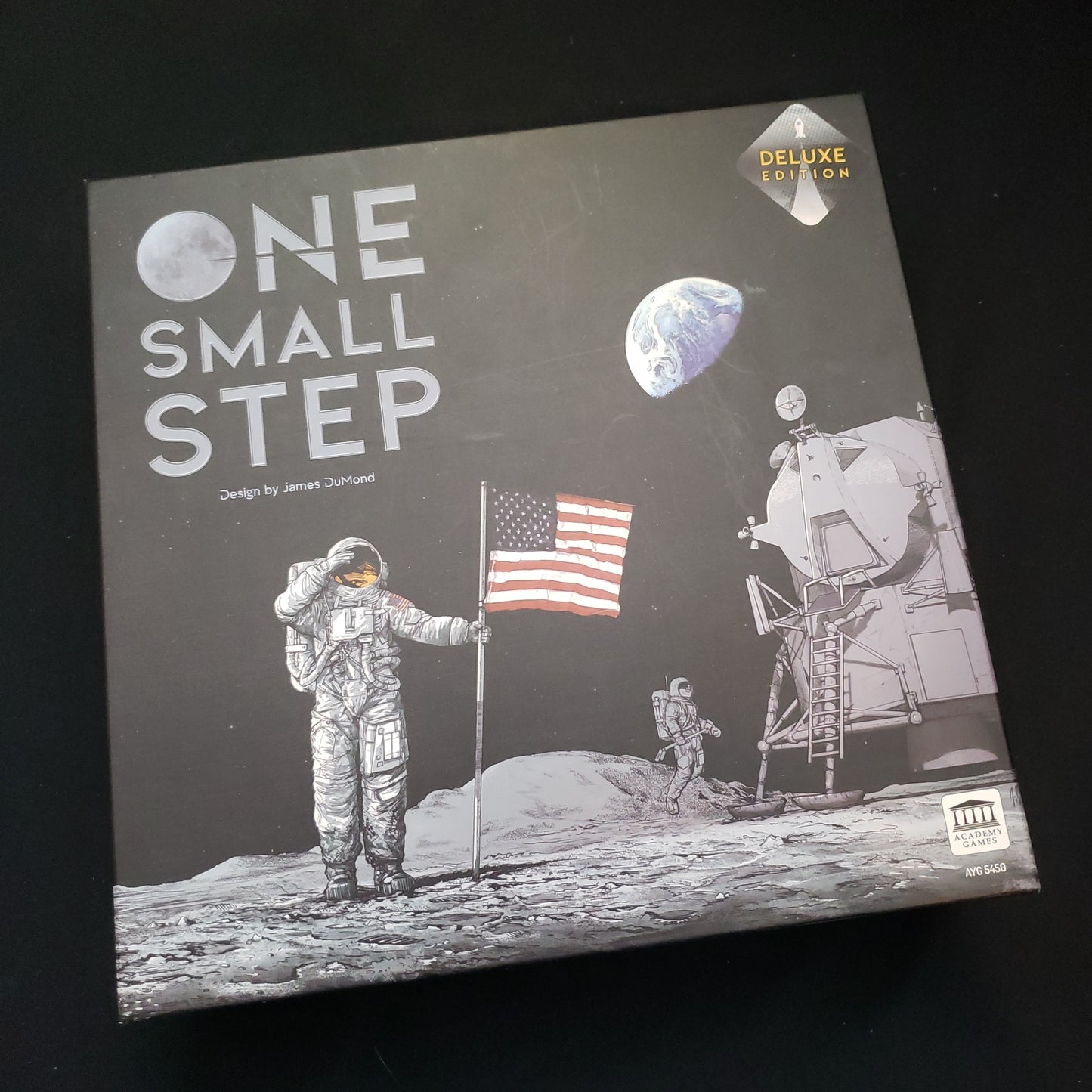 Image shows the front cover of the box of the One Small Step (Deluxe Edition board game