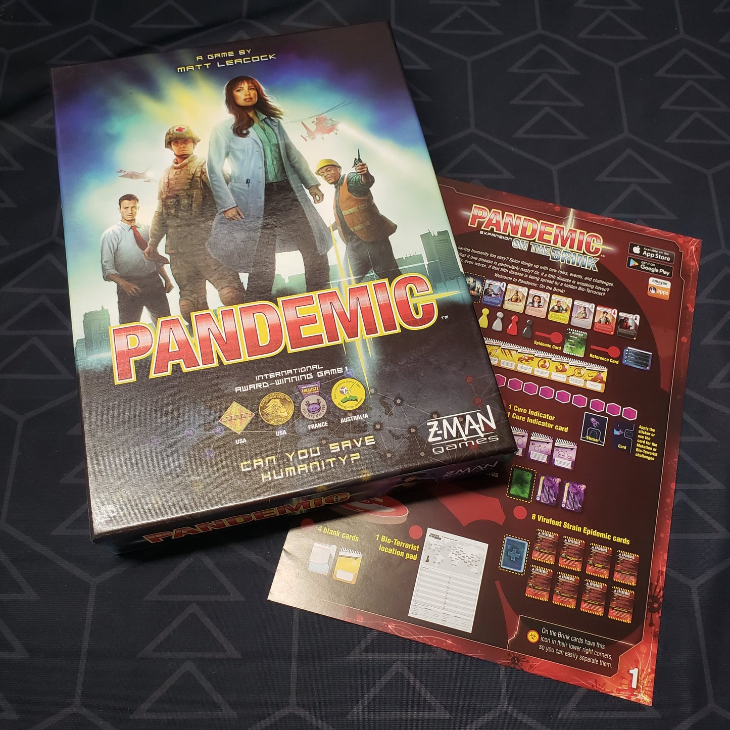 Image shows the front cover of the box of the Pandemic board game sitting on top of the instructions for the On The Brink expansion