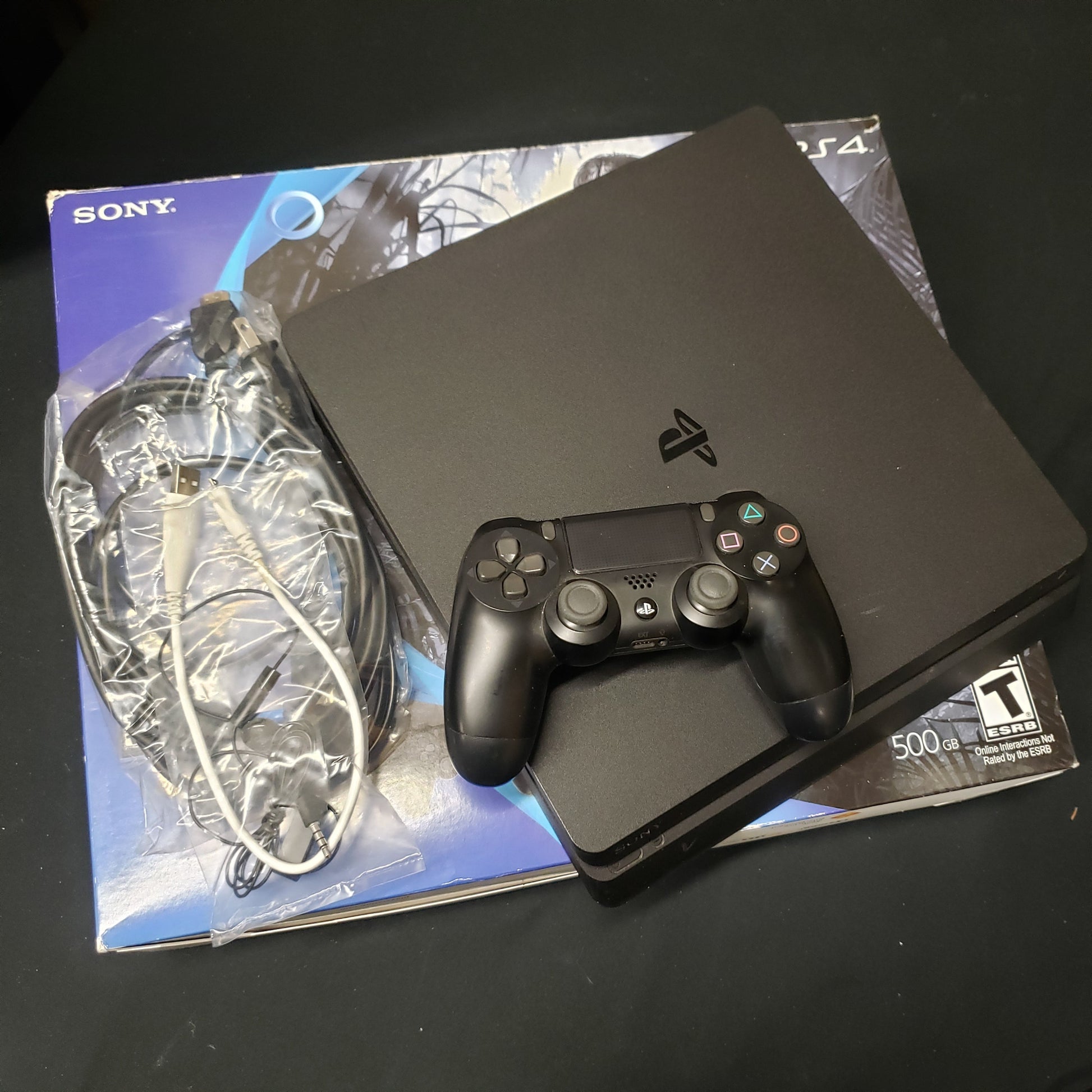 Image shows slim Playstation 4 console sitting on top its box with a controller and cables
