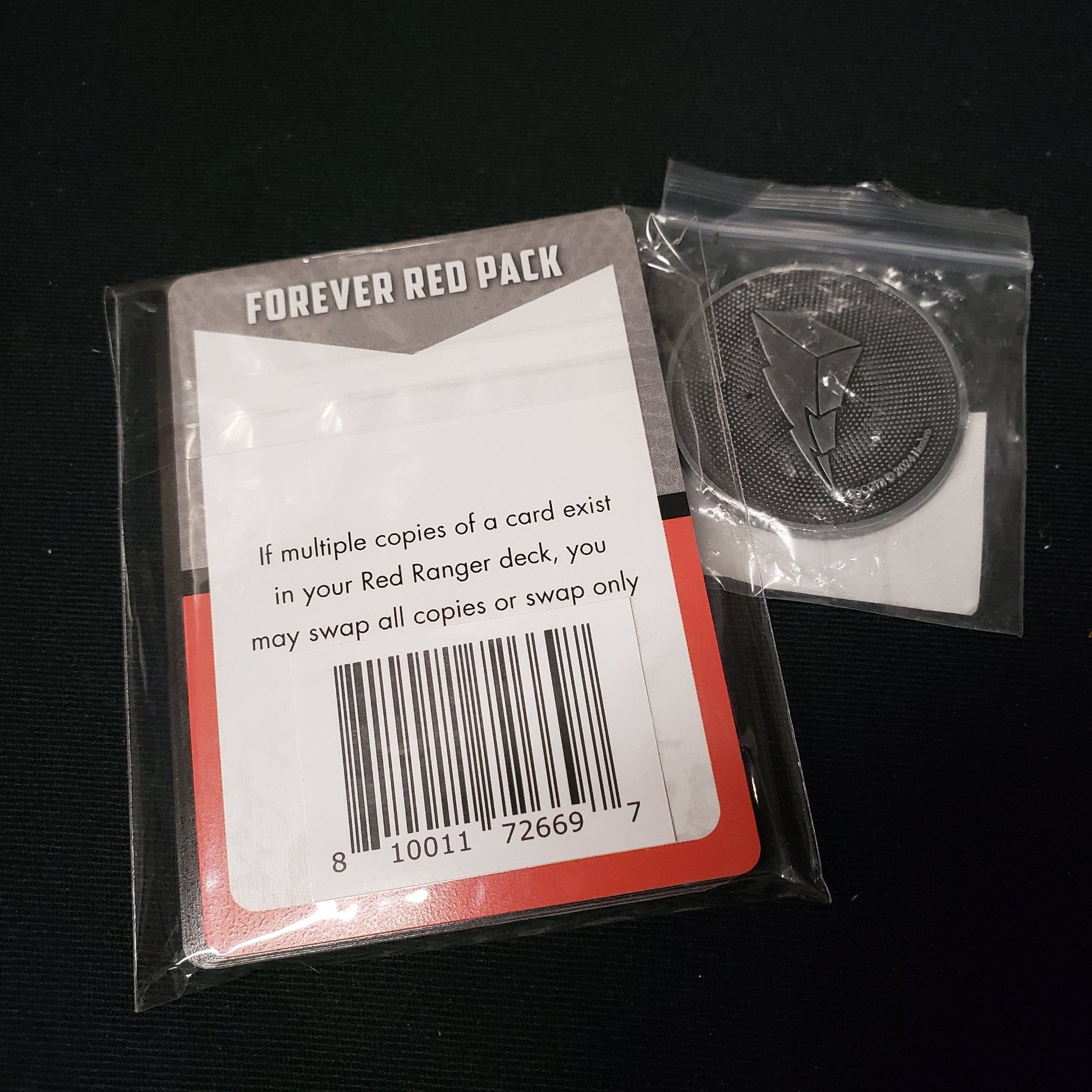 Image shows the Forever Red Promo Pack & a promo coin for the board game Power Rangers: Heroes of the Grid