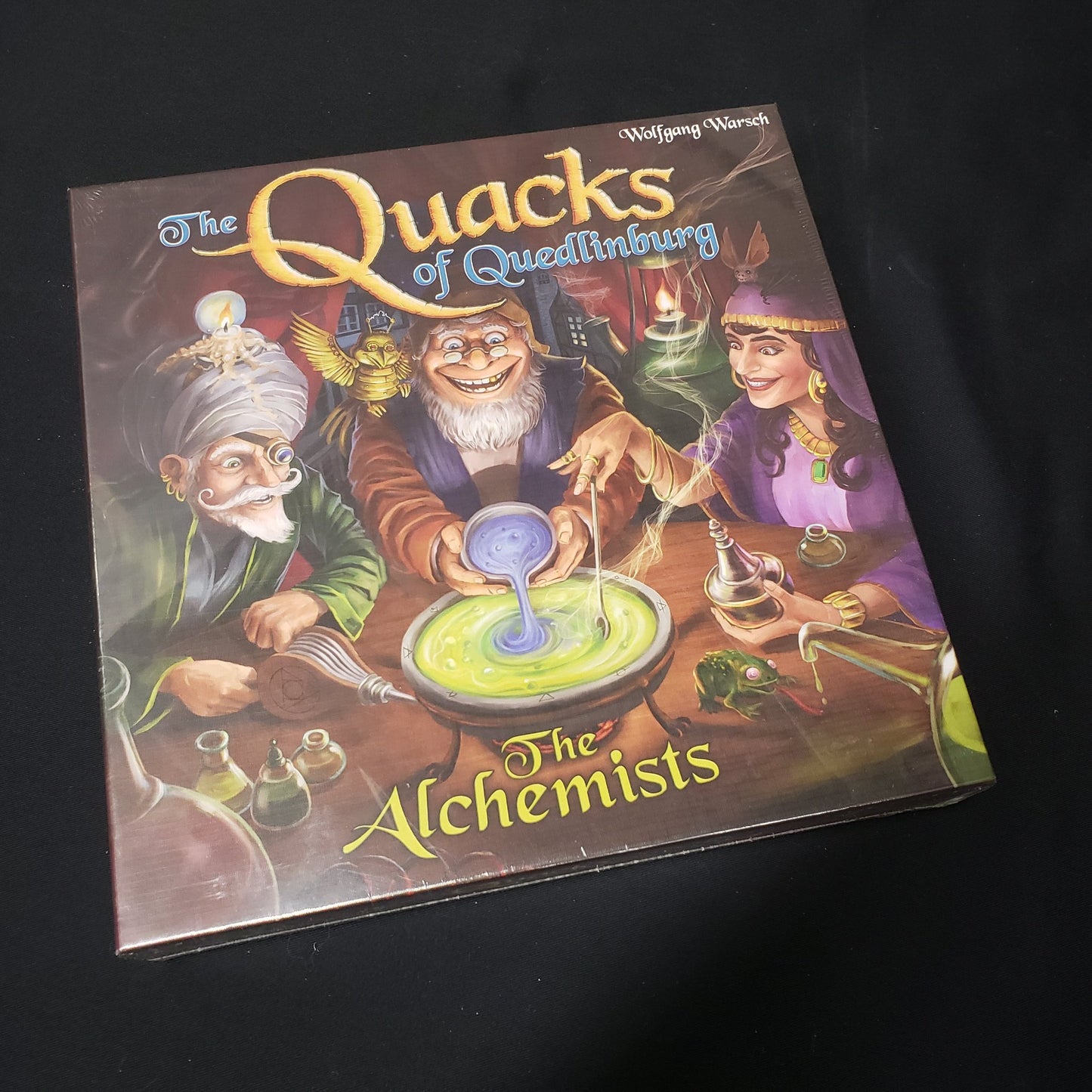 Image shows the front cover of the box of the Alchemists expansion for the board game Quacks of Quedlinburg
