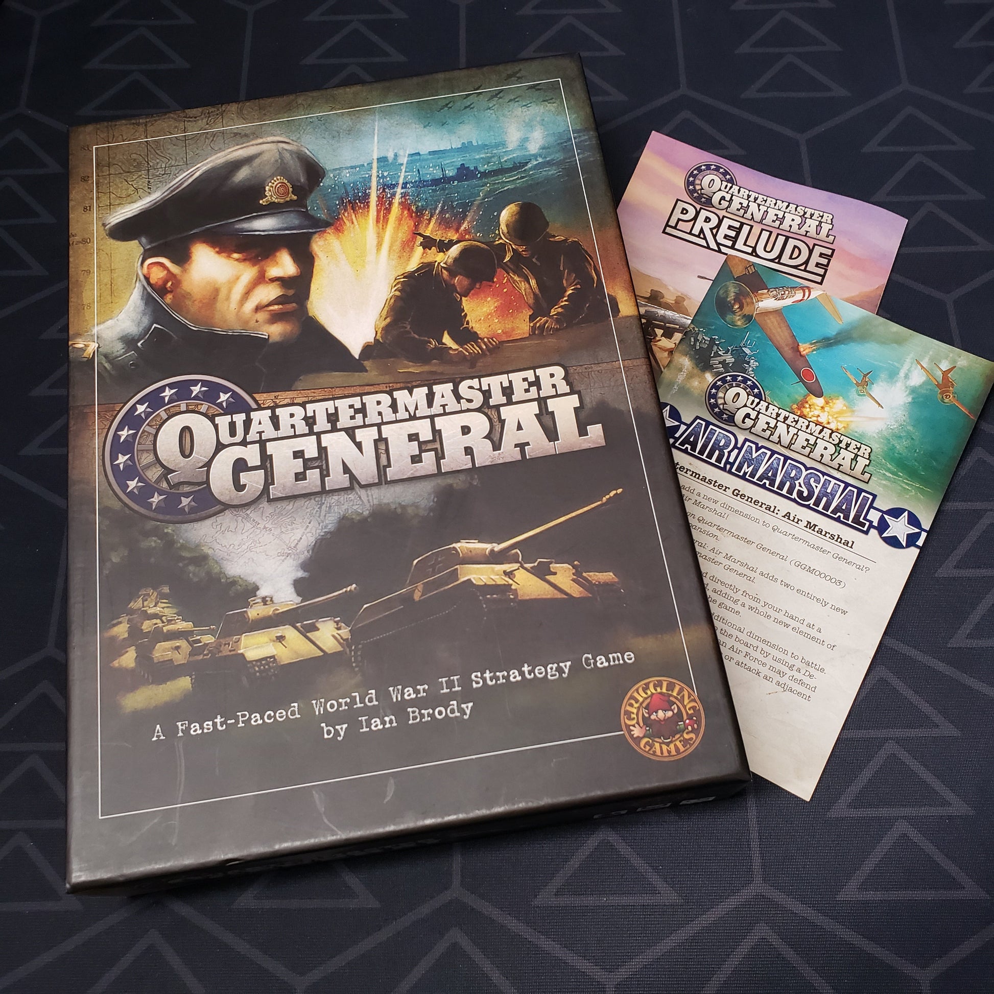 Image shows the front cover of the box of the Quartermaster General board game, with the instructions for the Air Marshal and Prelude expansions tucked underneath the box